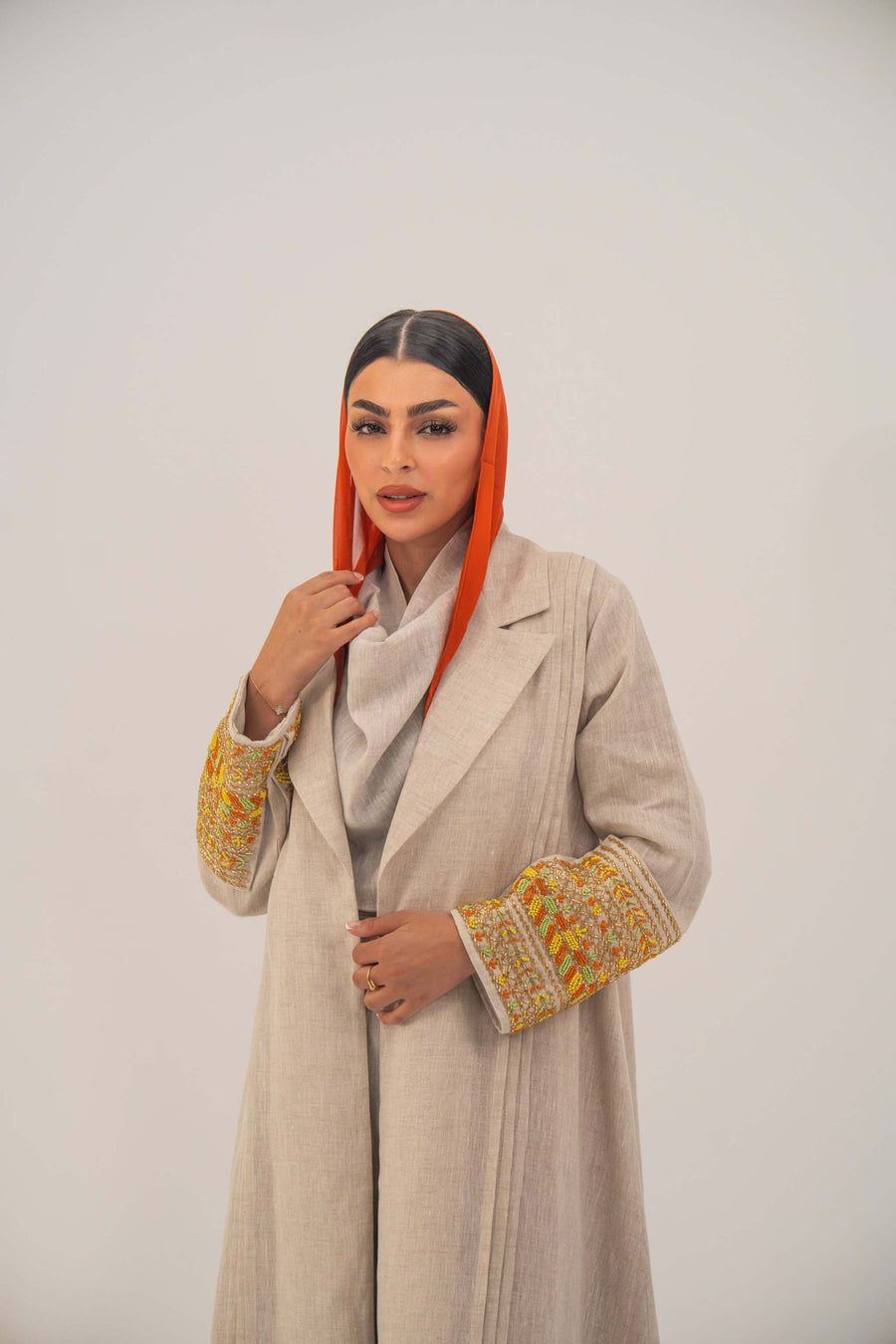 Beige linen blend abaya with tailored blazer-style cut, vibrant orange, gold, and green embroidery on sleeves, and subtle orange chiffon lining - sophisticated abaya