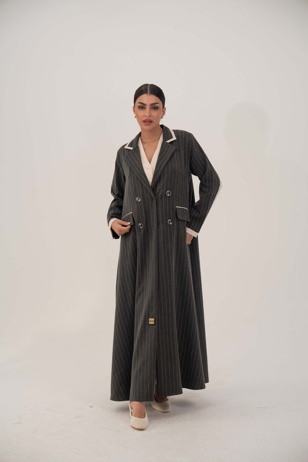 Woman wearing elegant black pinstriped blazer-style abaya with white lapels and cuffs, double-breasted design, and full-length hem.
