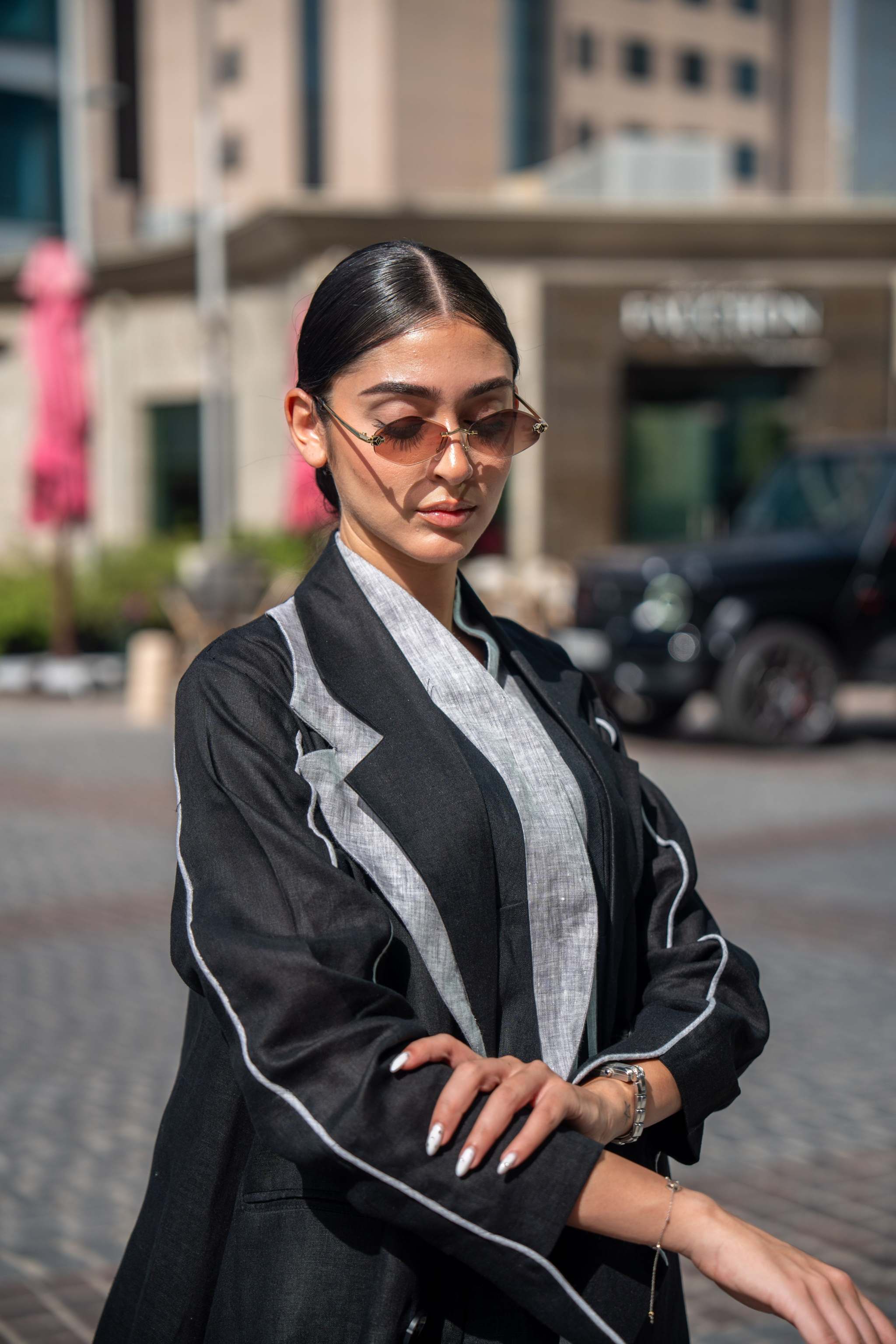 Woman wearing a black blazer abaya with white piping and sharp lapels in an urban setting