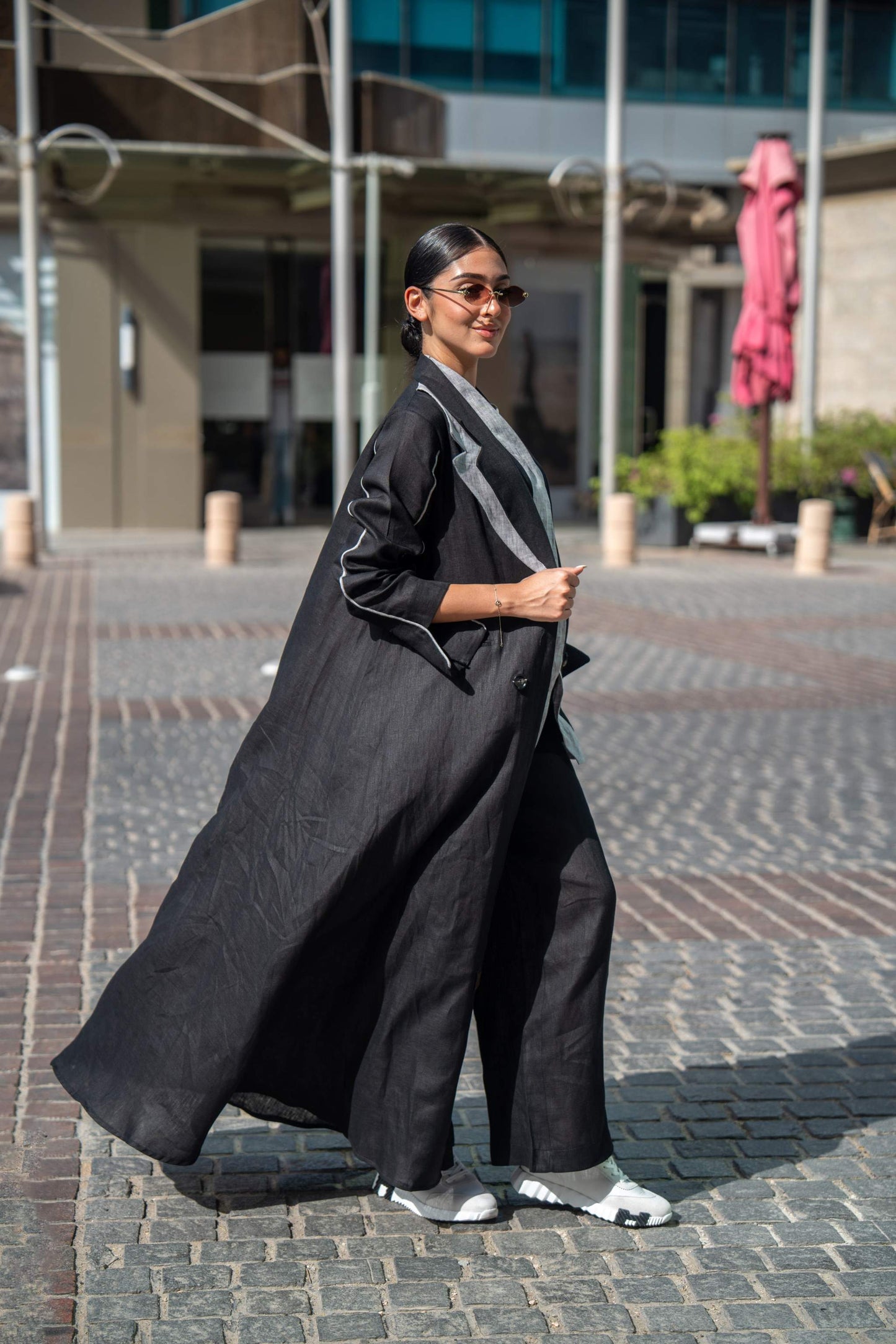 Woman wearing a black tailored blazer abaya with sharp lapels and white piping walking outdoors