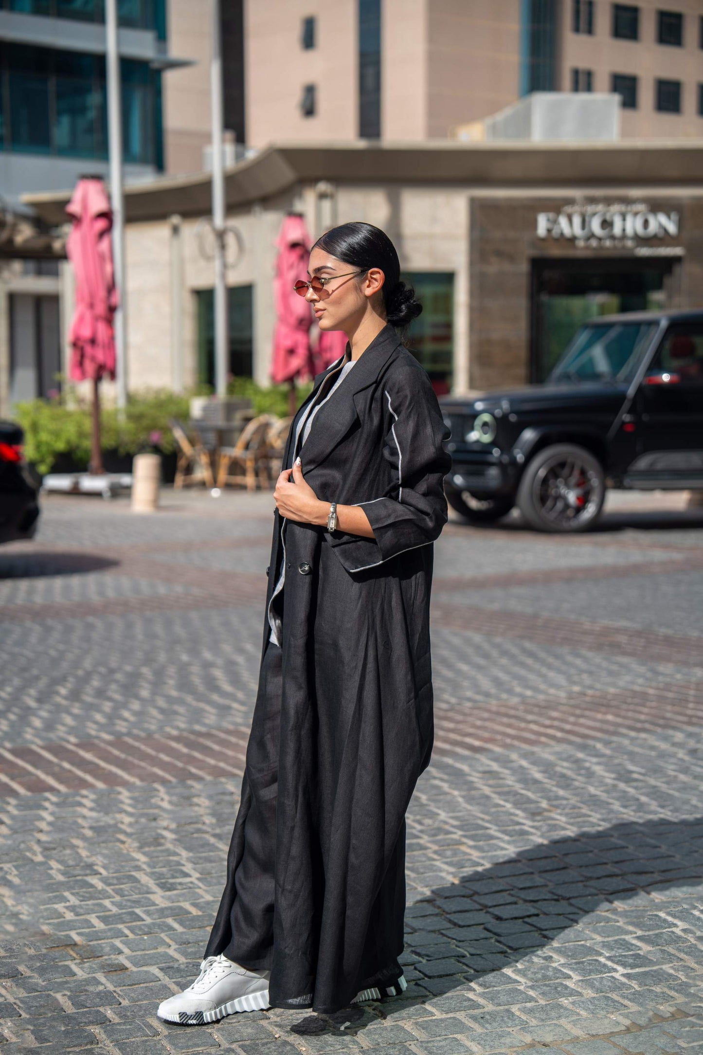 Woman wearing black blazer abaya with sharp lapels and white piping in urban setting