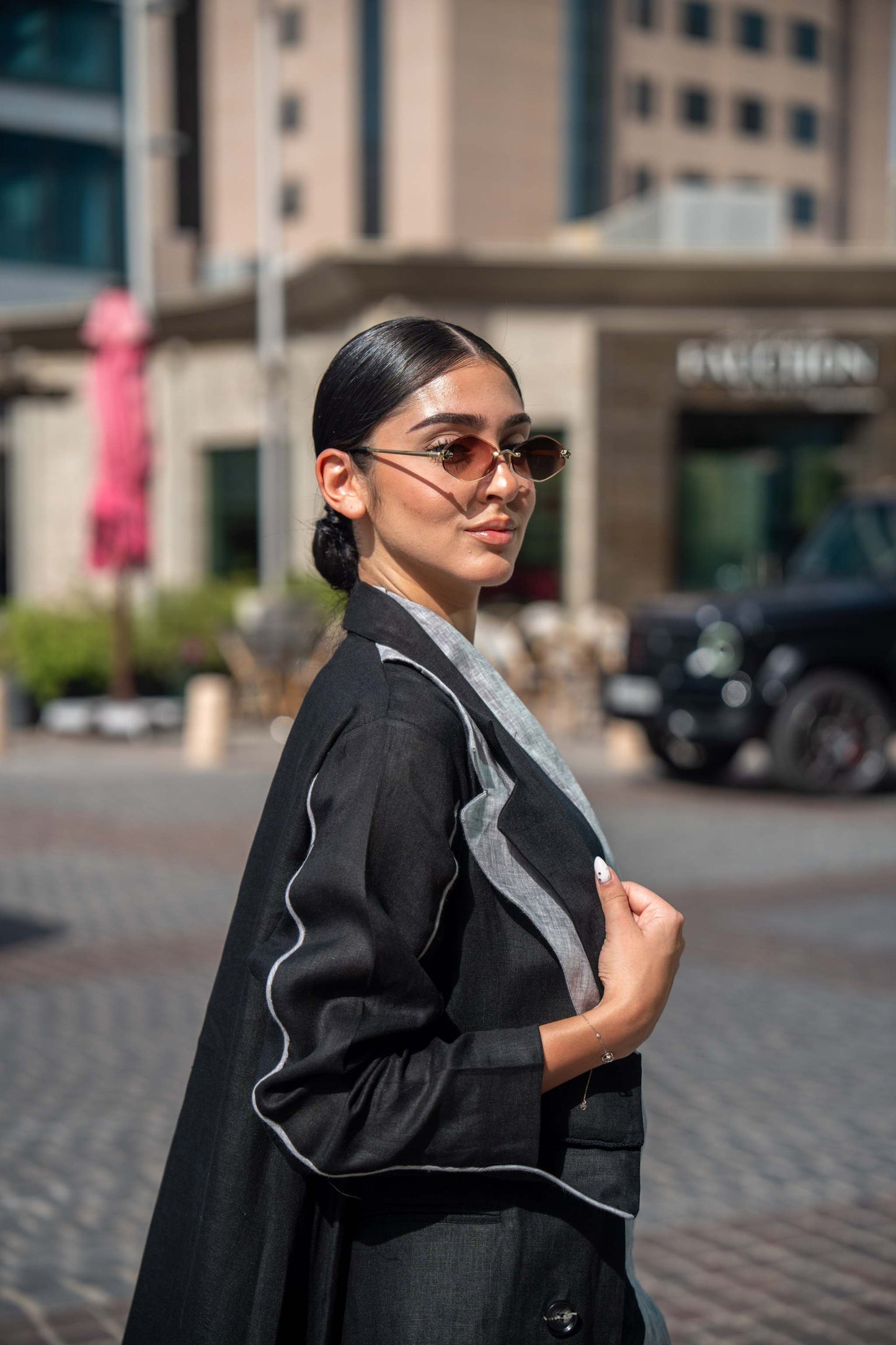 Woman wearing black blazer abaya with white piping and sharp lapels in urban street setting