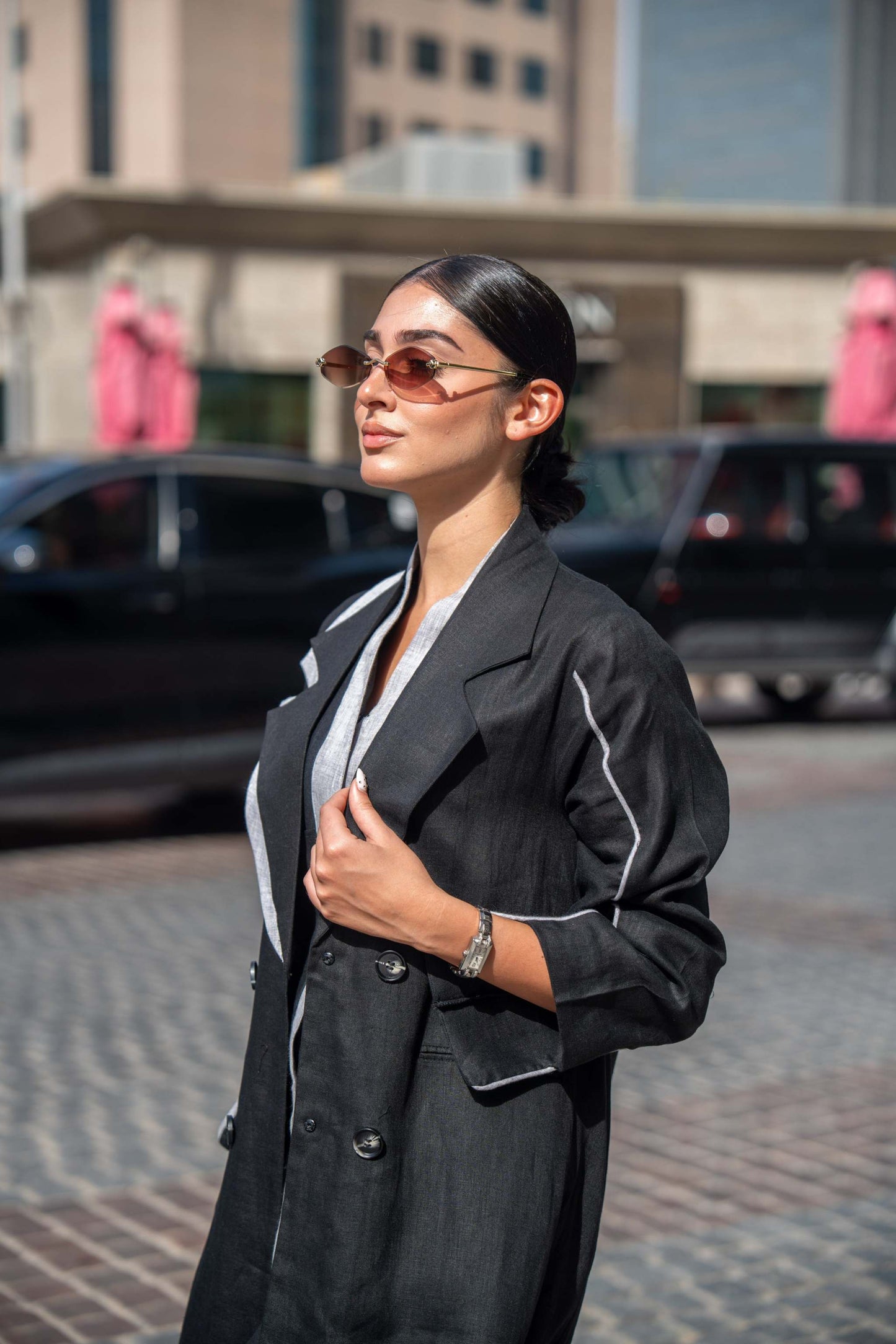 Woman wearing black blazer abaya with sharp lapels and white piping, styled for professional and casual settings outdoors