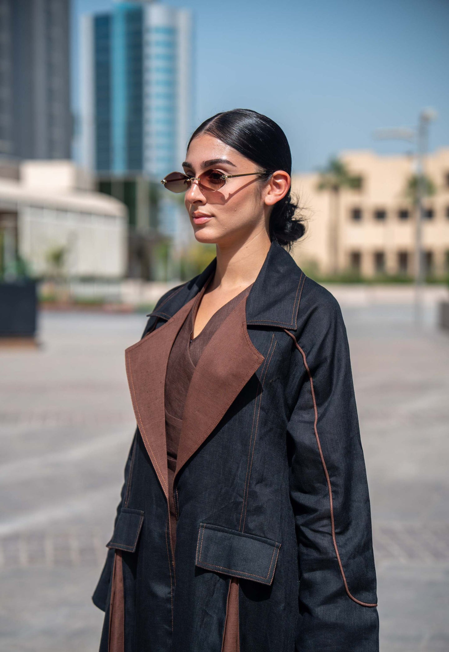Woman wearing a modern black and brown linen Velora abaya with wide lapels and clean lines in an urban setting