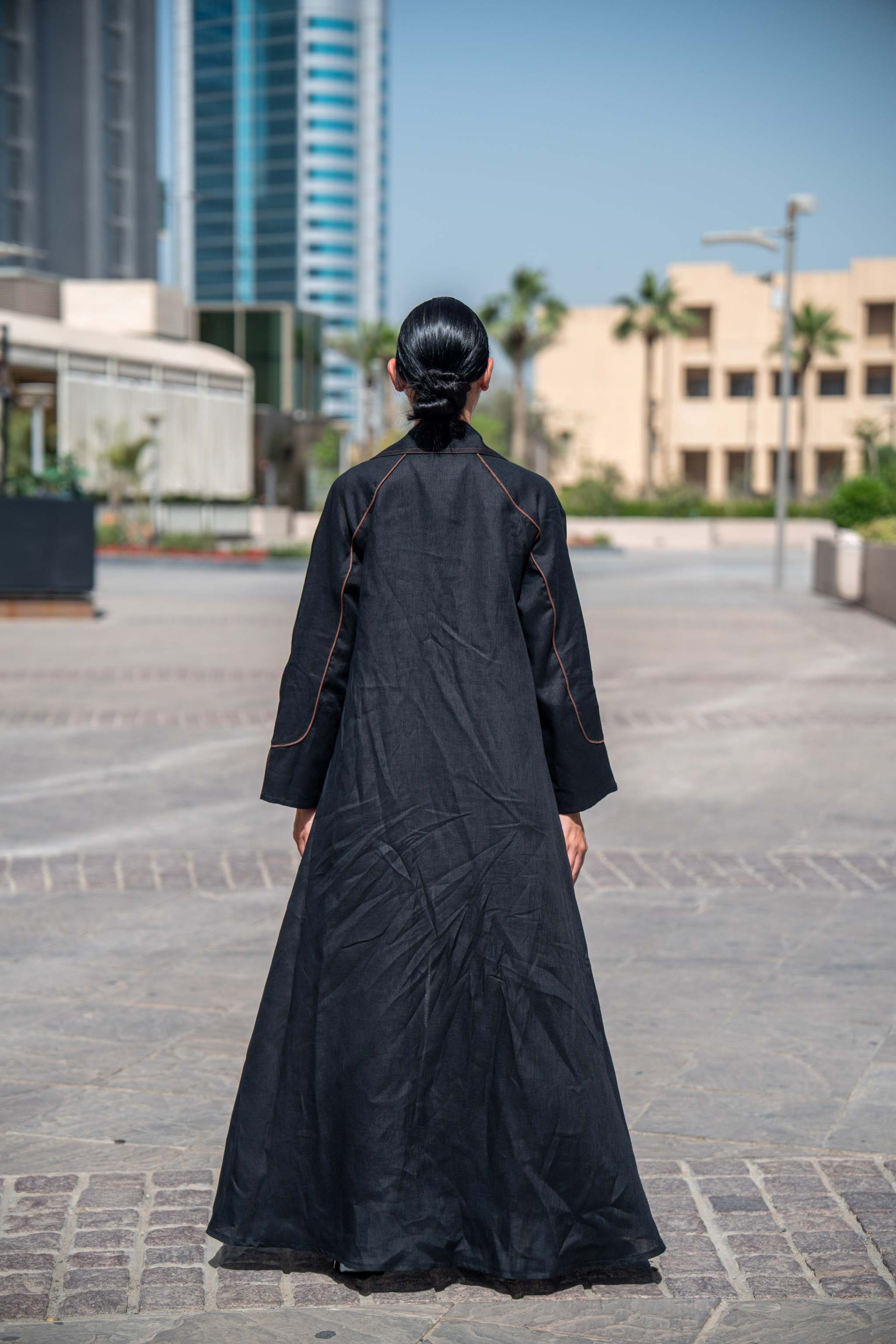 Back view of a woman wearing a black and brown linen Velora abaya with wide lapels and clean lines in an urban setting