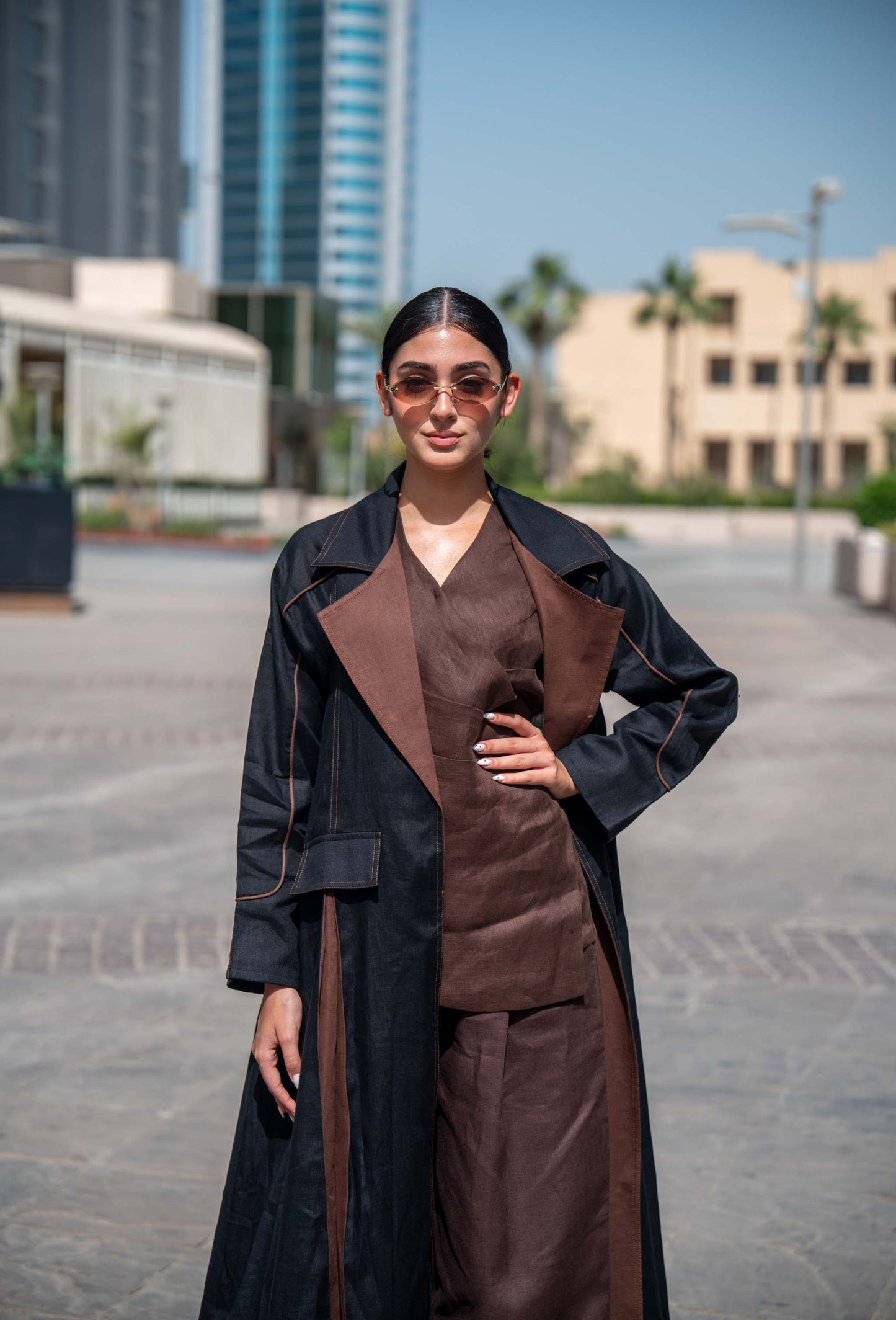 Woman wearing a contemporary abaya in black and brown linen with wide lapels and clean lines, standing outdoors in an urban setting.