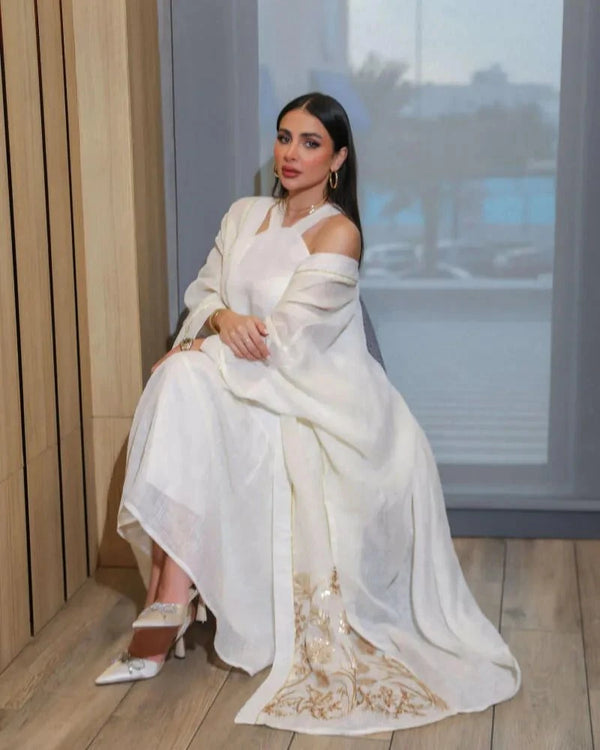 woman wearing lightweight white inner dress with long sheer embroidered outer layer sitting indoors
