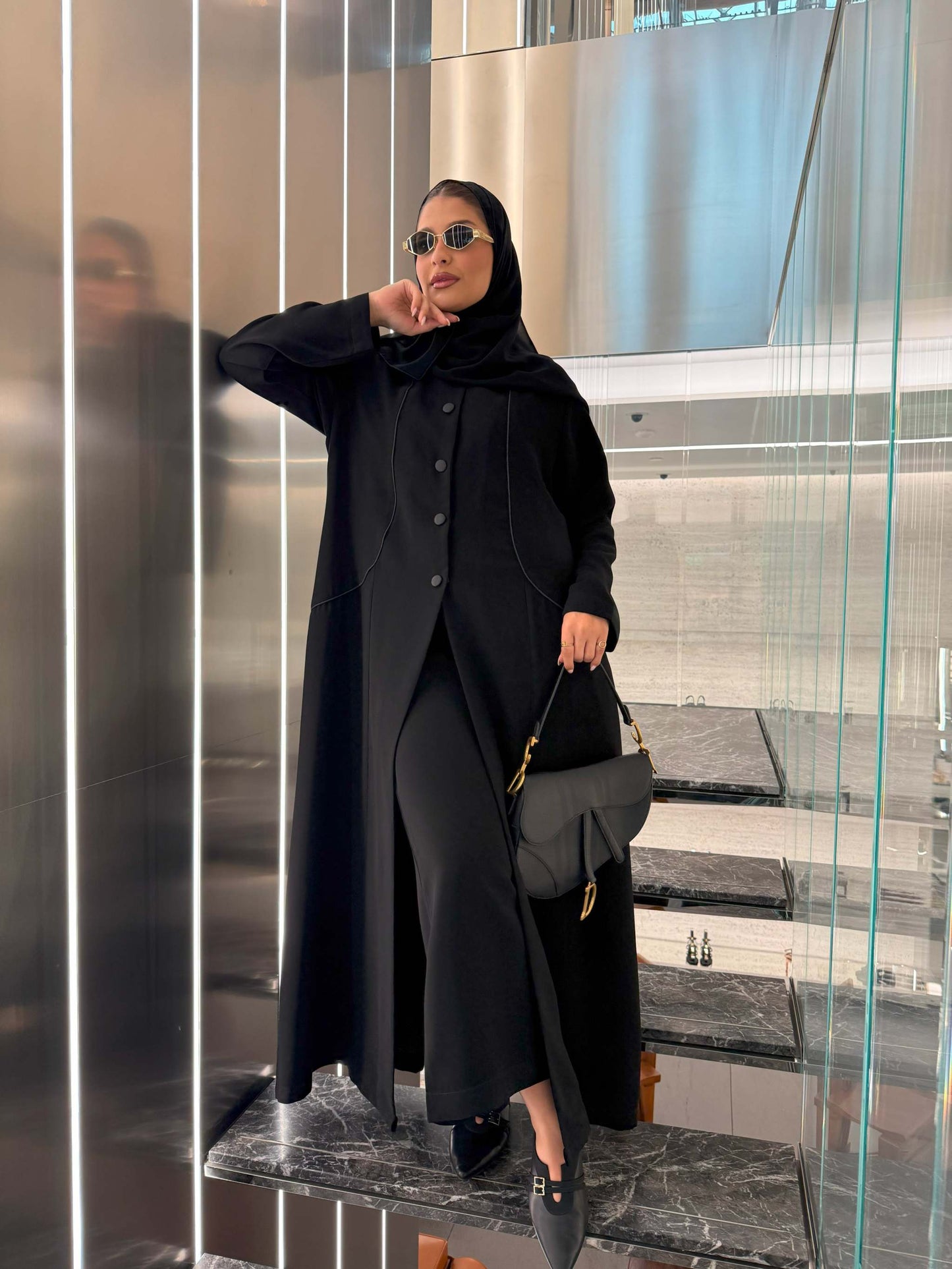 Black crepe blazer-style abaya with silk lining, structured buttons, and subtle seam detailing worn with sunglasses and black handbag.