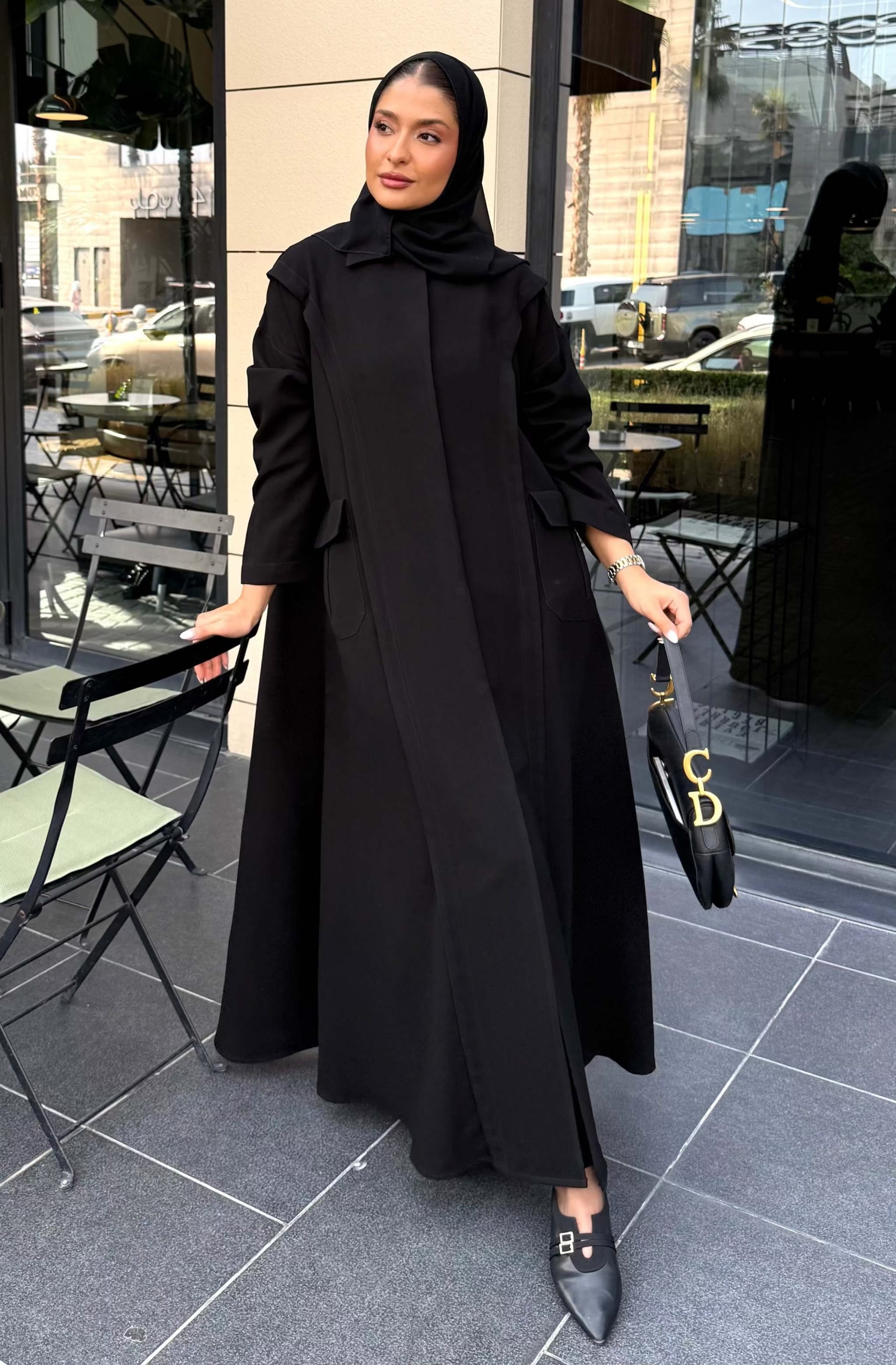 Woman wearing a black abaya with a straight cut and holding a handbag outdoors