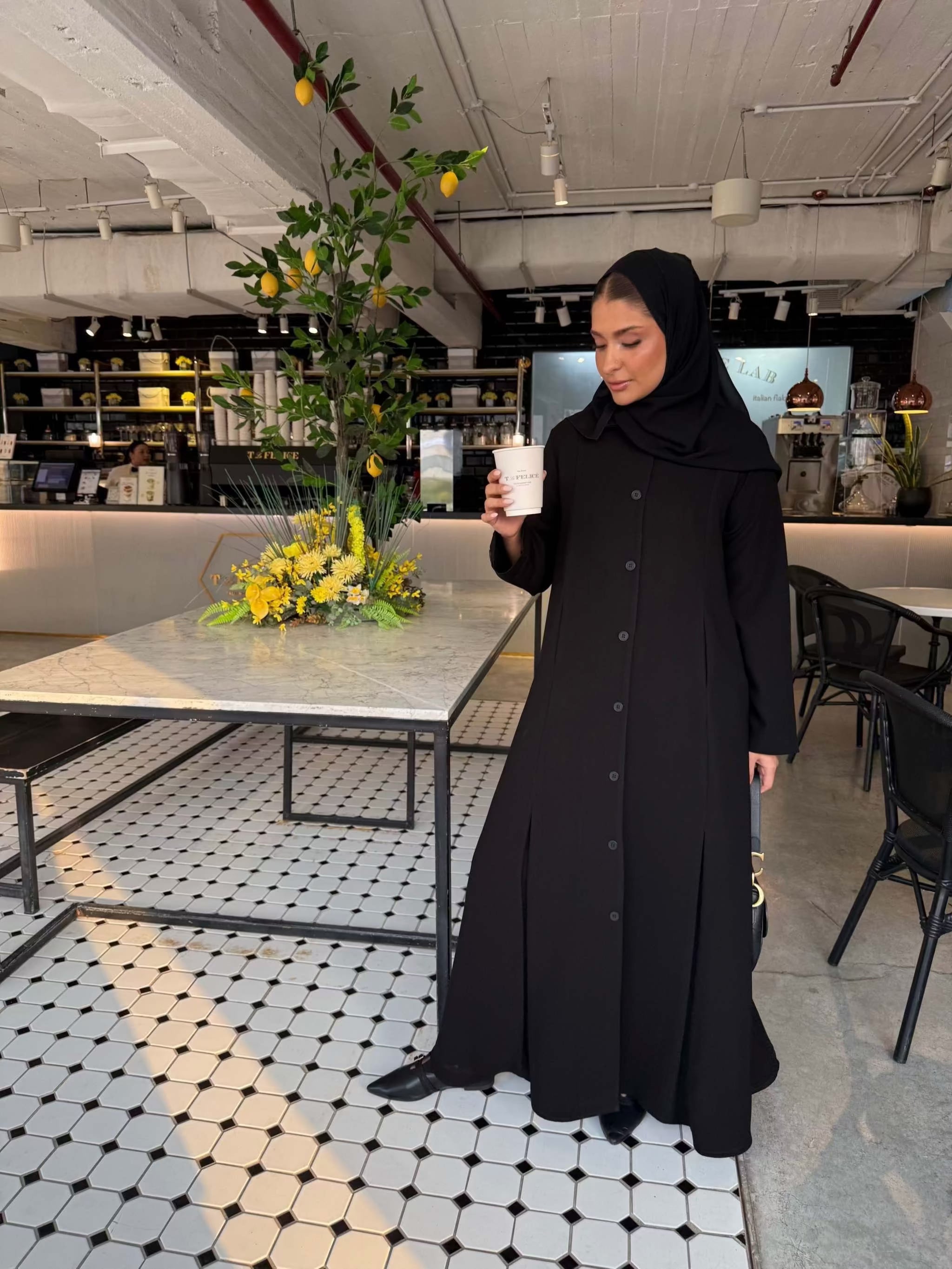 Elegant black crepe abaya with button-down front and subtle pleated skirt detail, worn with a black hijab - The Sophisticated Crepe Abaya