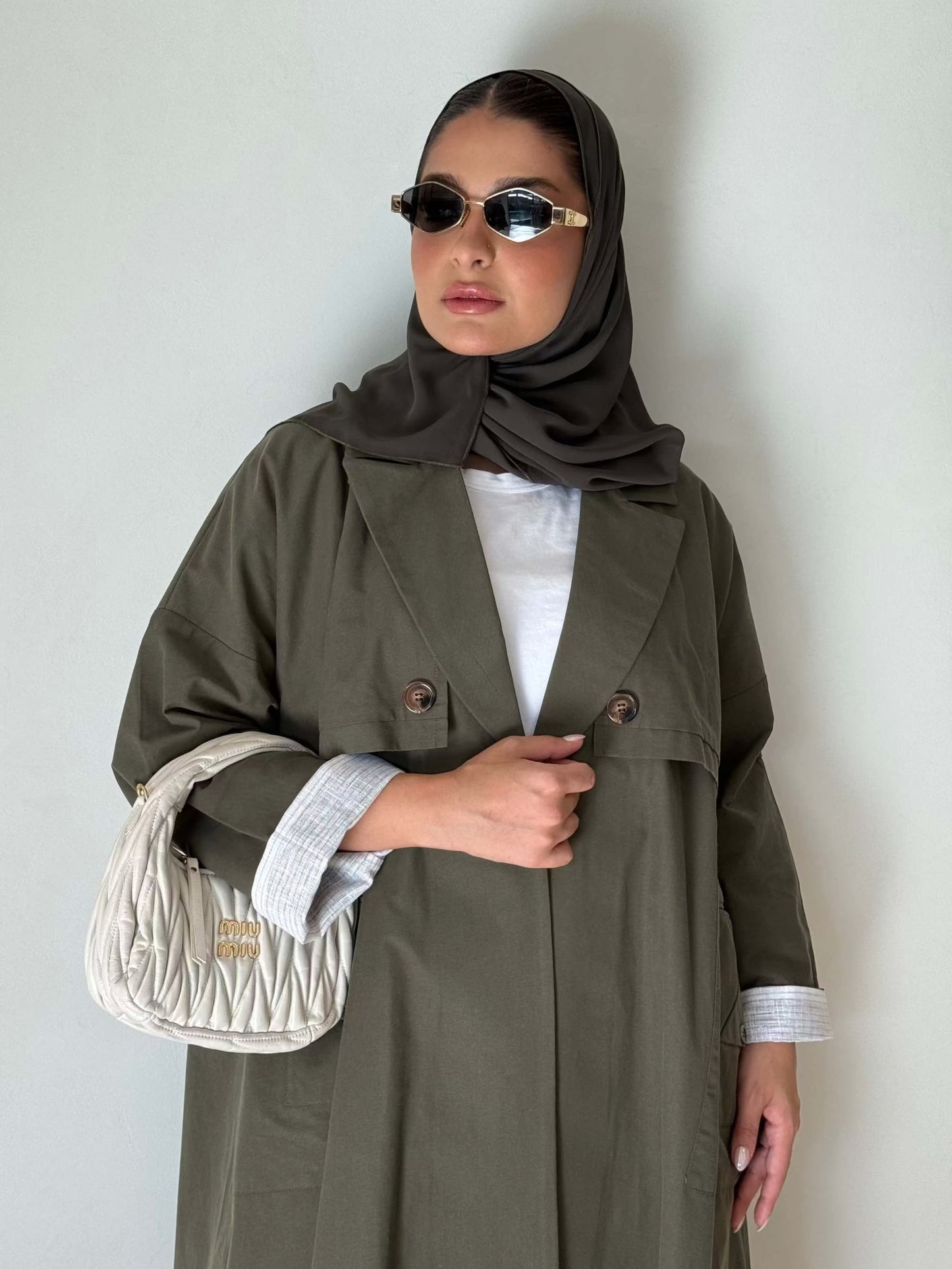 The Modern Khaki crepe trench abaya with button-up front and structured collar worn with sunglasses and hijab