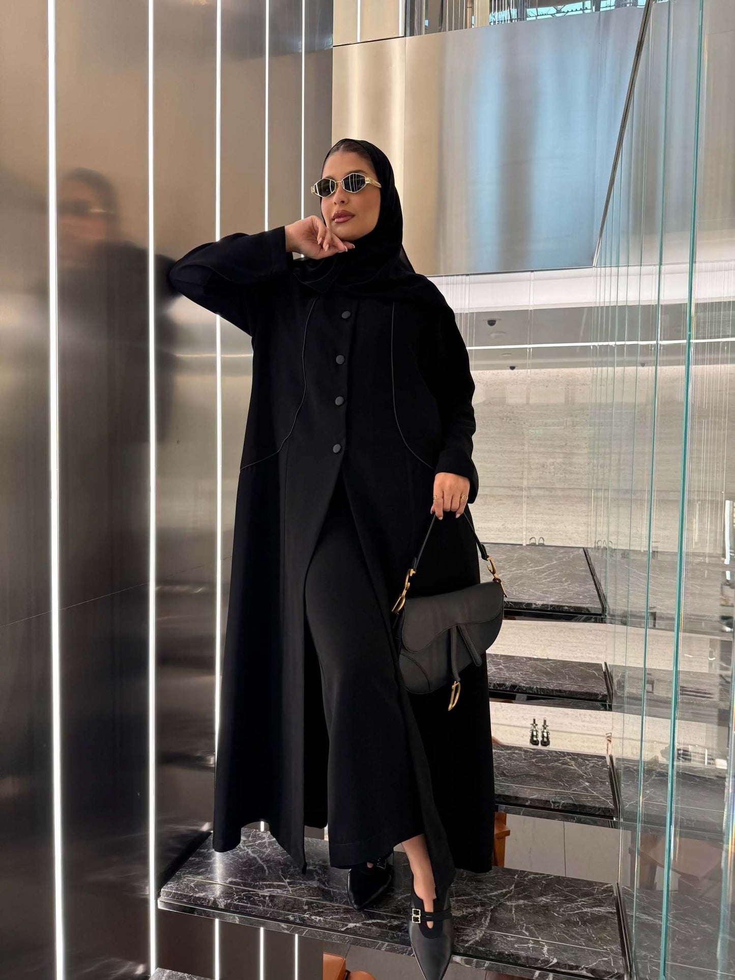 Elegant black crepe abaya with luxurious silk lining and tailored silhouette worn with sunglasses and handbag.