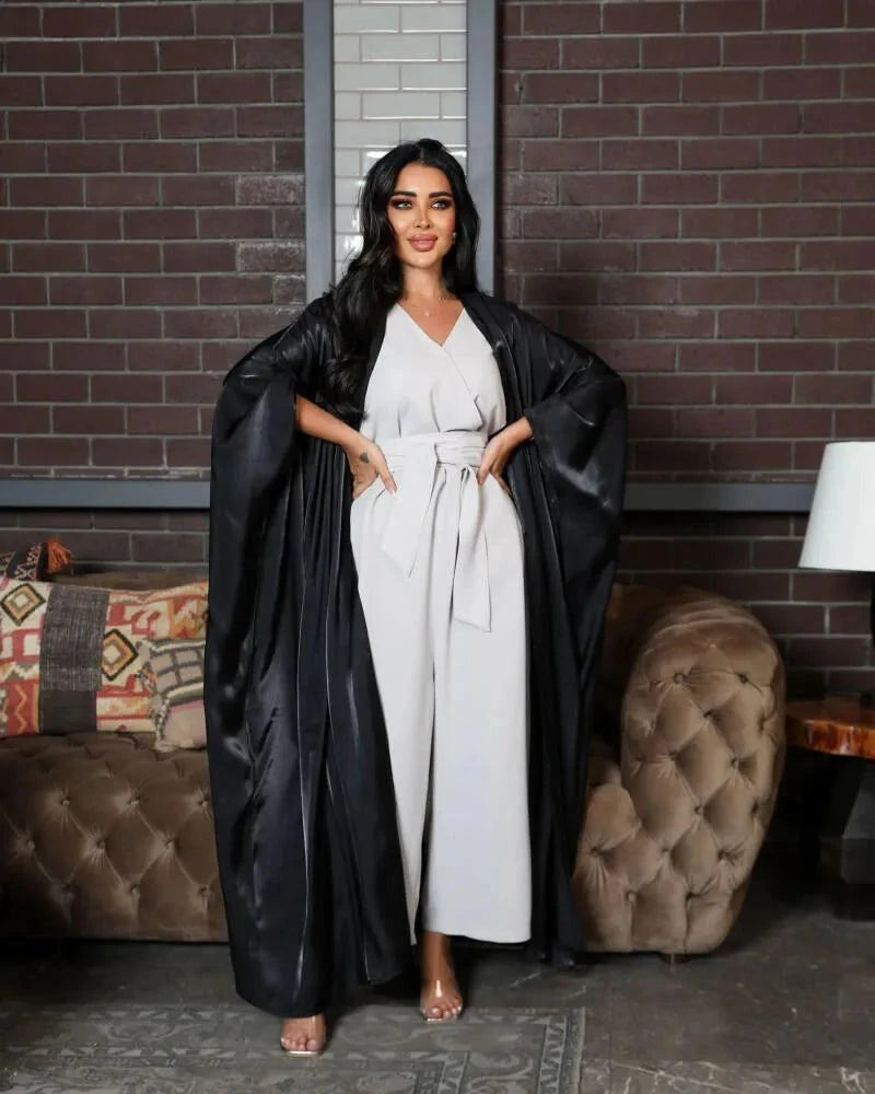 Woman wearing a luxurious black bisht made of shimmering silk fabric over a white outfit in a stylish indoor setting