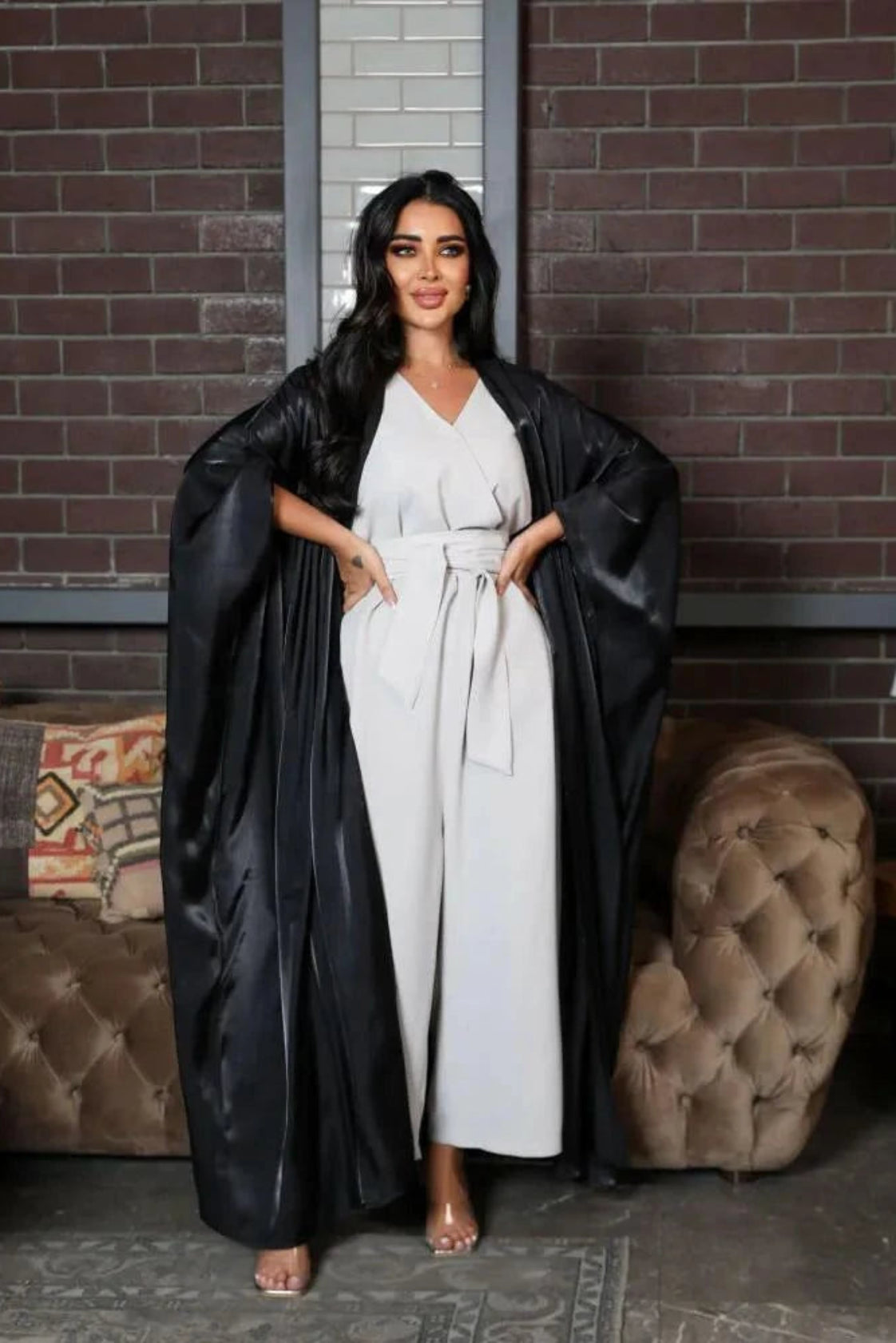 Woman wearing a luxurious black bisht made of shimmering silk fabric over a white outfit in a stylish indoor setting