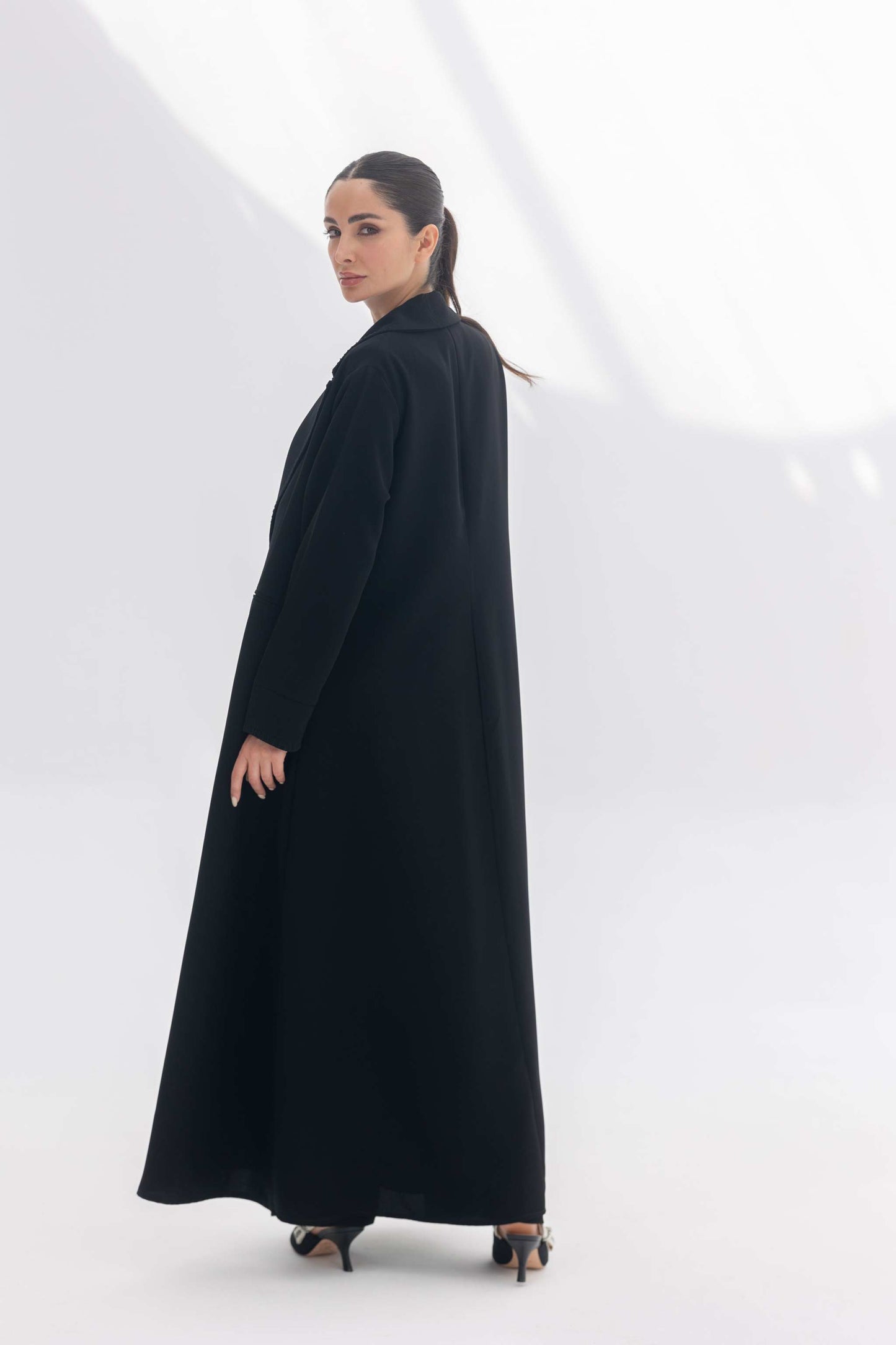 Woman wearing a black crepe blazer abaya with tailored silhouette and subtle embroidery, styled with matching black crepe inner and pants.