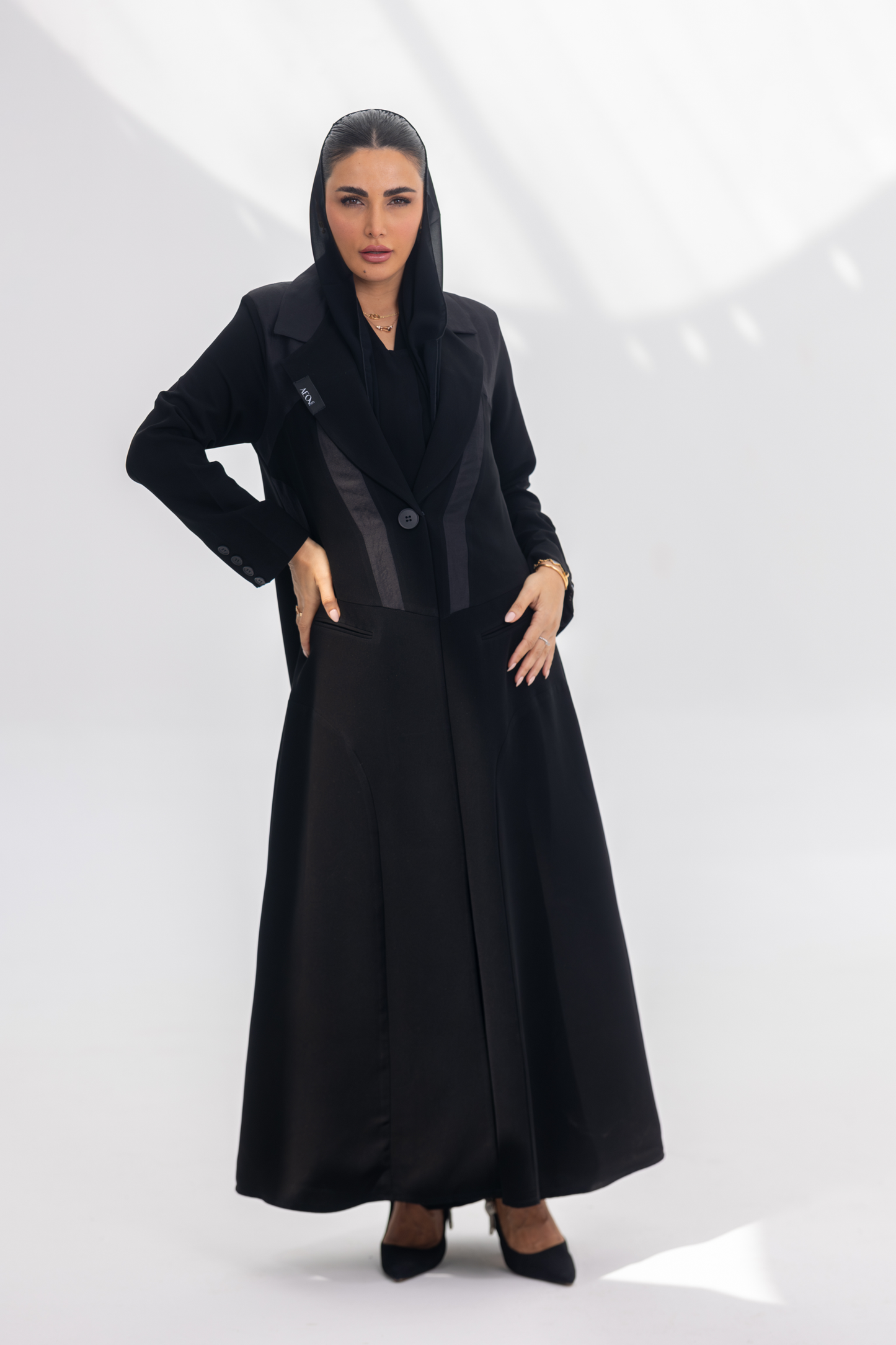 Woman wearing elegant black crepe abaya with dark grey accents and silk lining, standing in a bright, minimal setting