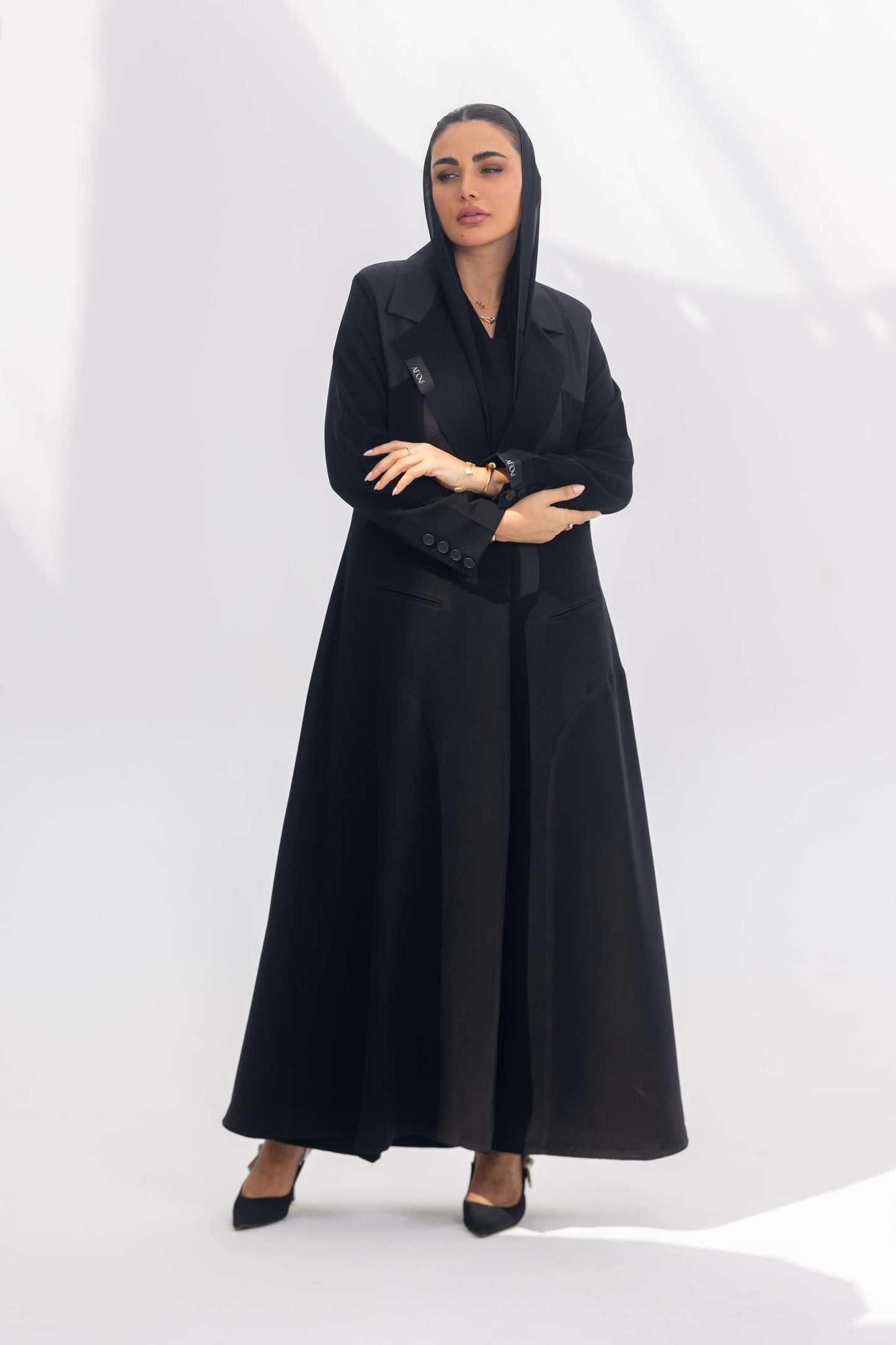 Woman wearing elegant black crepe abaya with dark grey accents and silk lining, standing confidently against white background