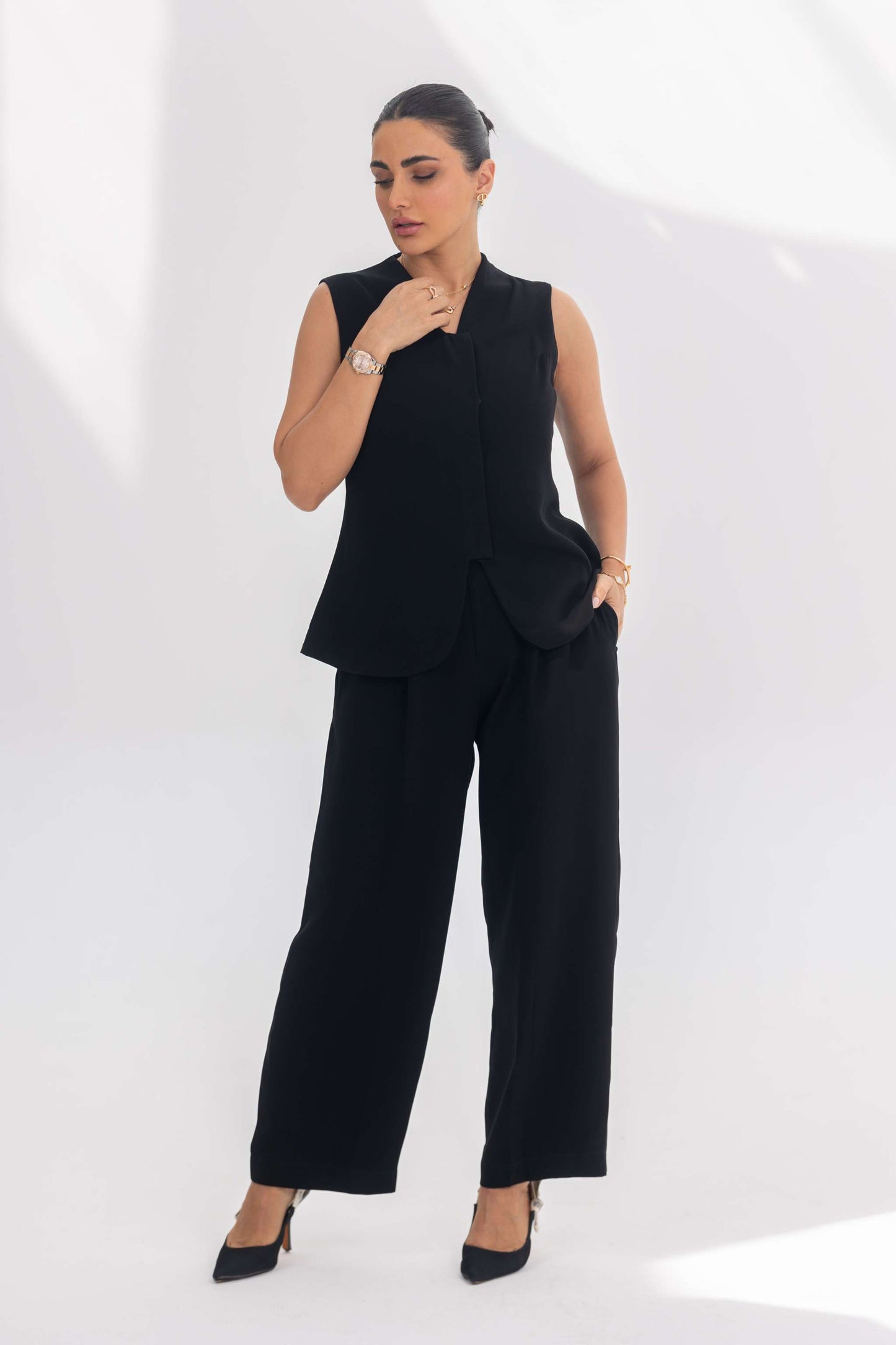 Woman wearing black sleeveless crepe inner set with wide-leg pants and black heels in bright studio setting