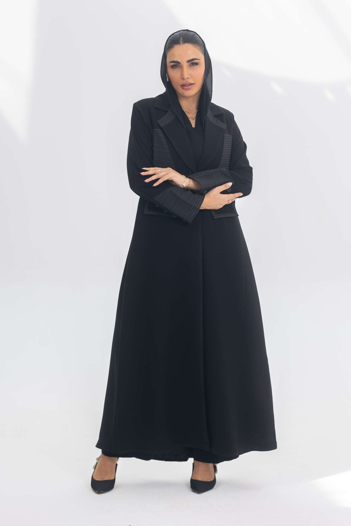 Woman wearing black crepe blazer abaya with contrasting textures, standing confidently against white background.