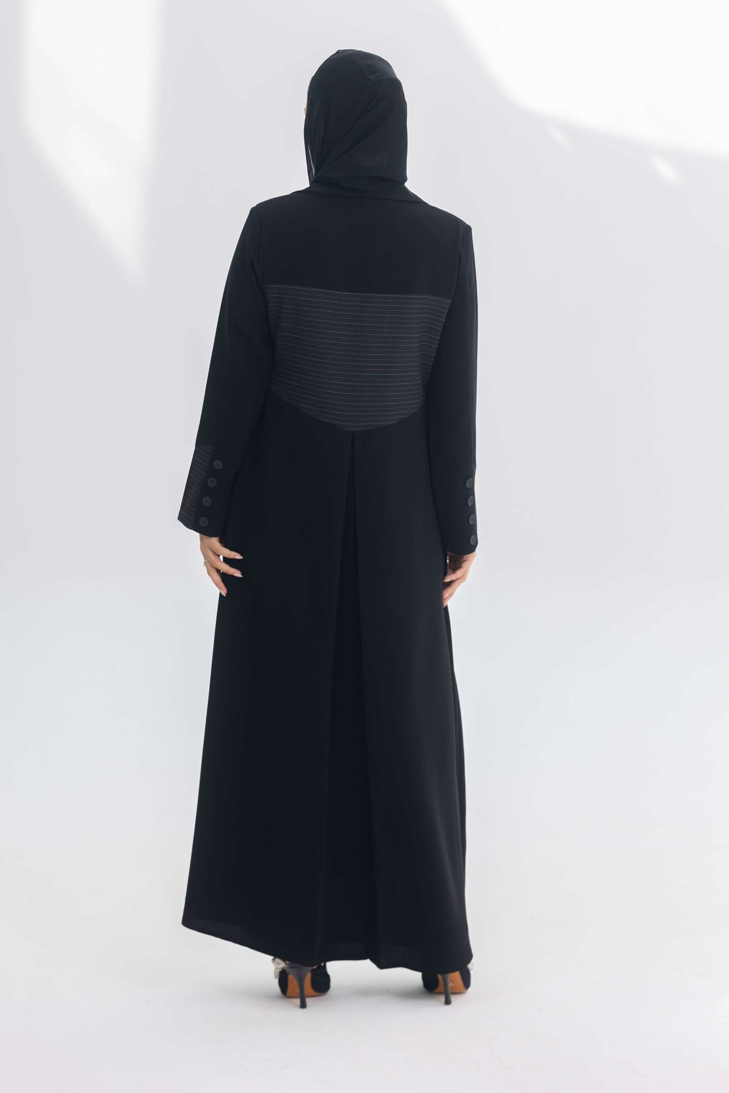 Woman wearing black crepe blazer abaya with contrasting back panel detail, standing against white background