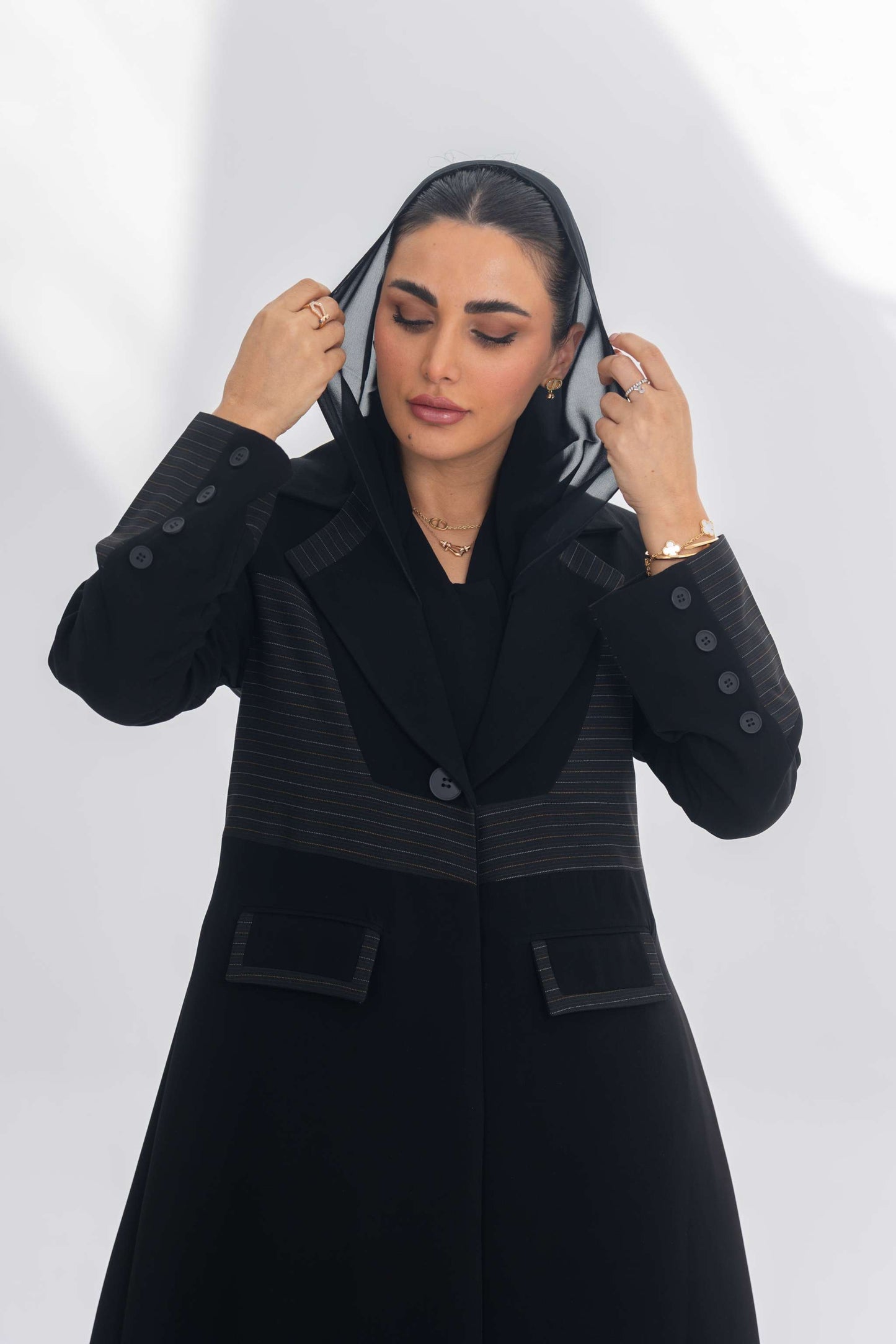 Black crepe blazer abaya with contrasting fabric detail, worn by woman adjusting hood, showcasing elegant modern design.