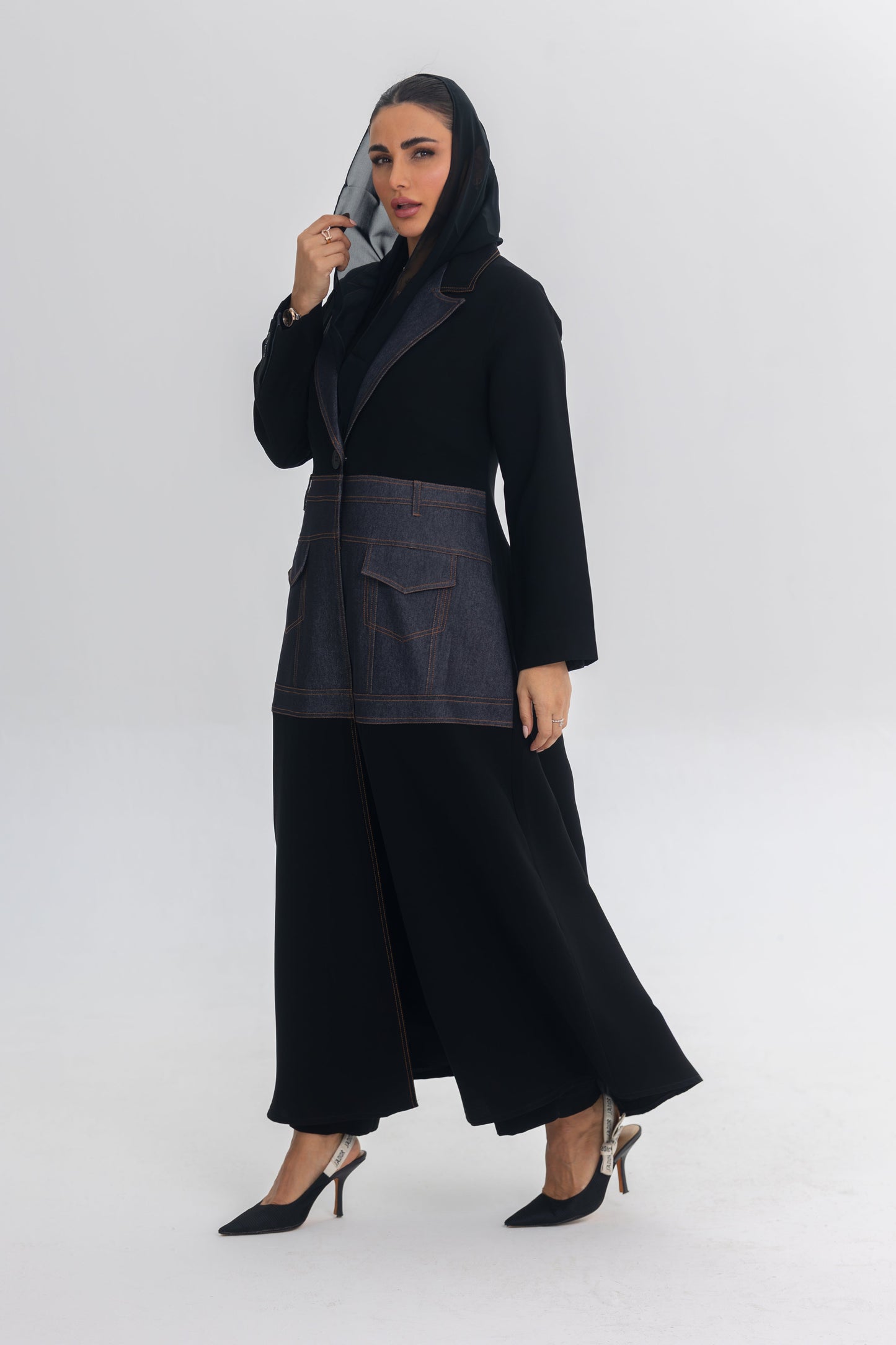 Woman wearing Blue Stitch black crepe abaya with denim fabric details and blue stitching, styled with black heels and a black headscarf.