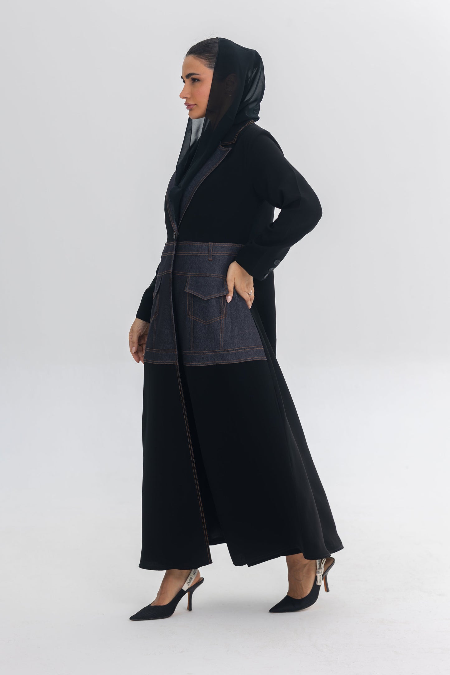 Woman wearing a black crepe abaya with blue denim stitch detail and hooded scarf