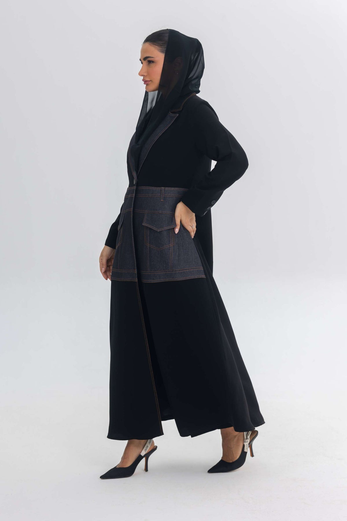 Woman wearing a black crepe abaya with blue denim stitch detail and hooded scarf
