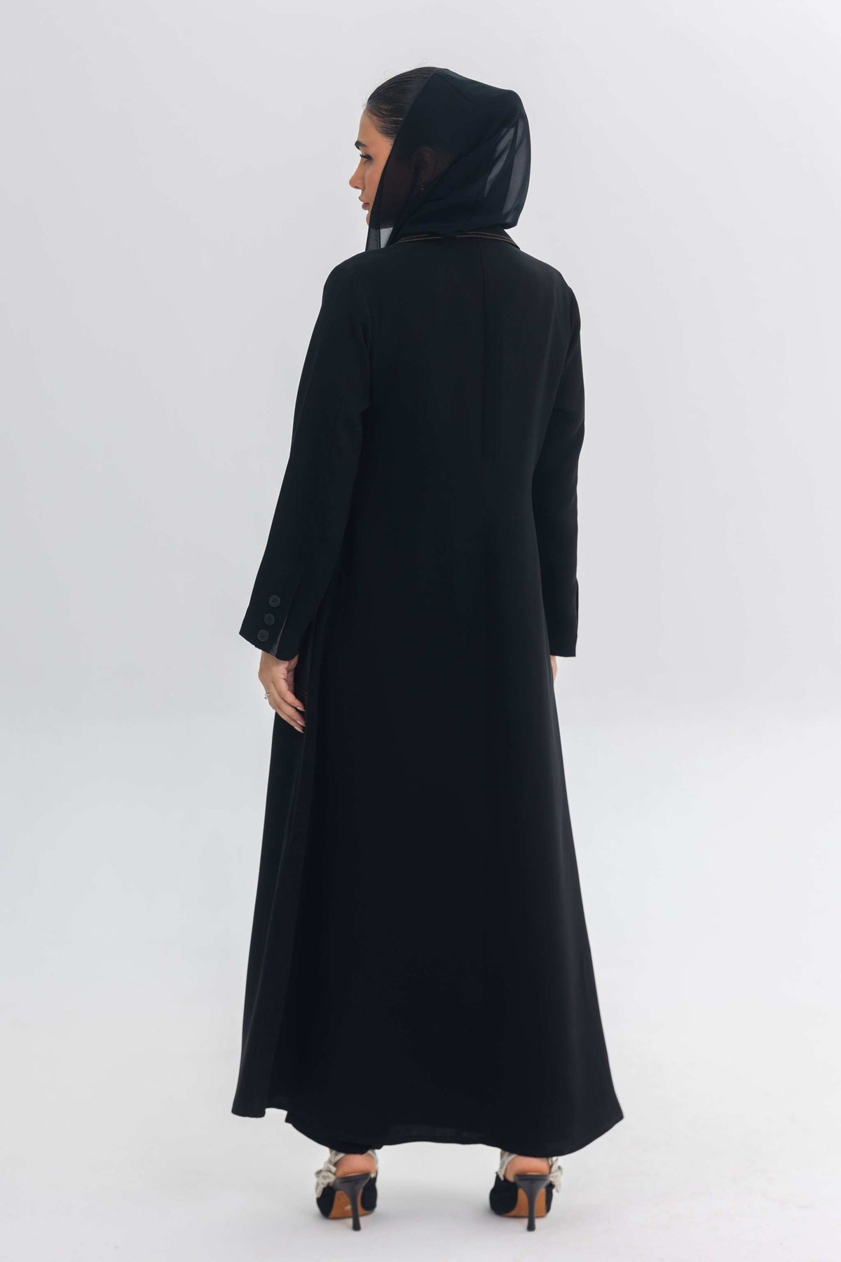 Back view of a woman wearing a sleek black crepe abaya with a hood, part of the Blue Stitch collection.