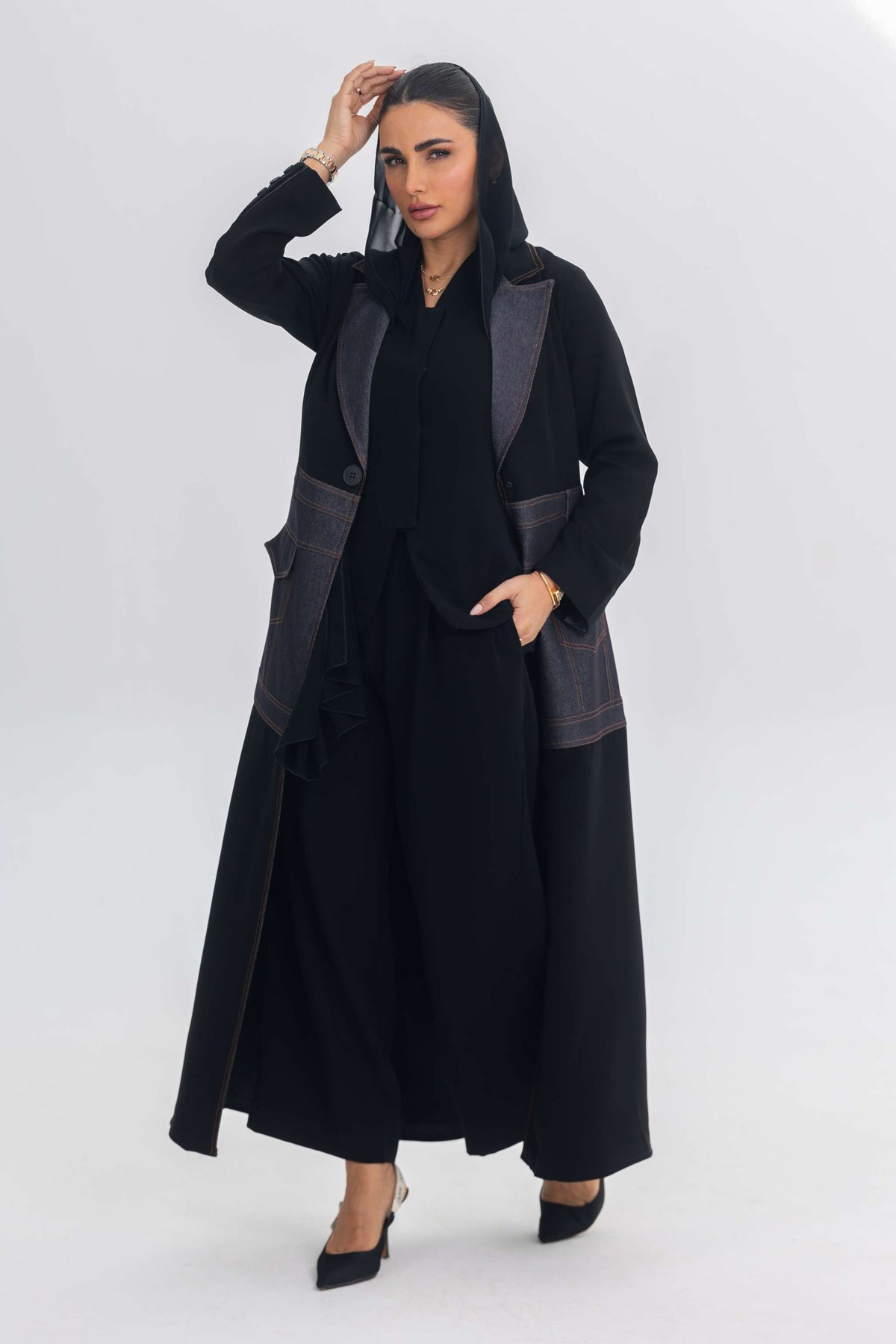 Woman wearing a black crepe abaya with denim fabric and blue stitch details, showcasing contemporary elegance.