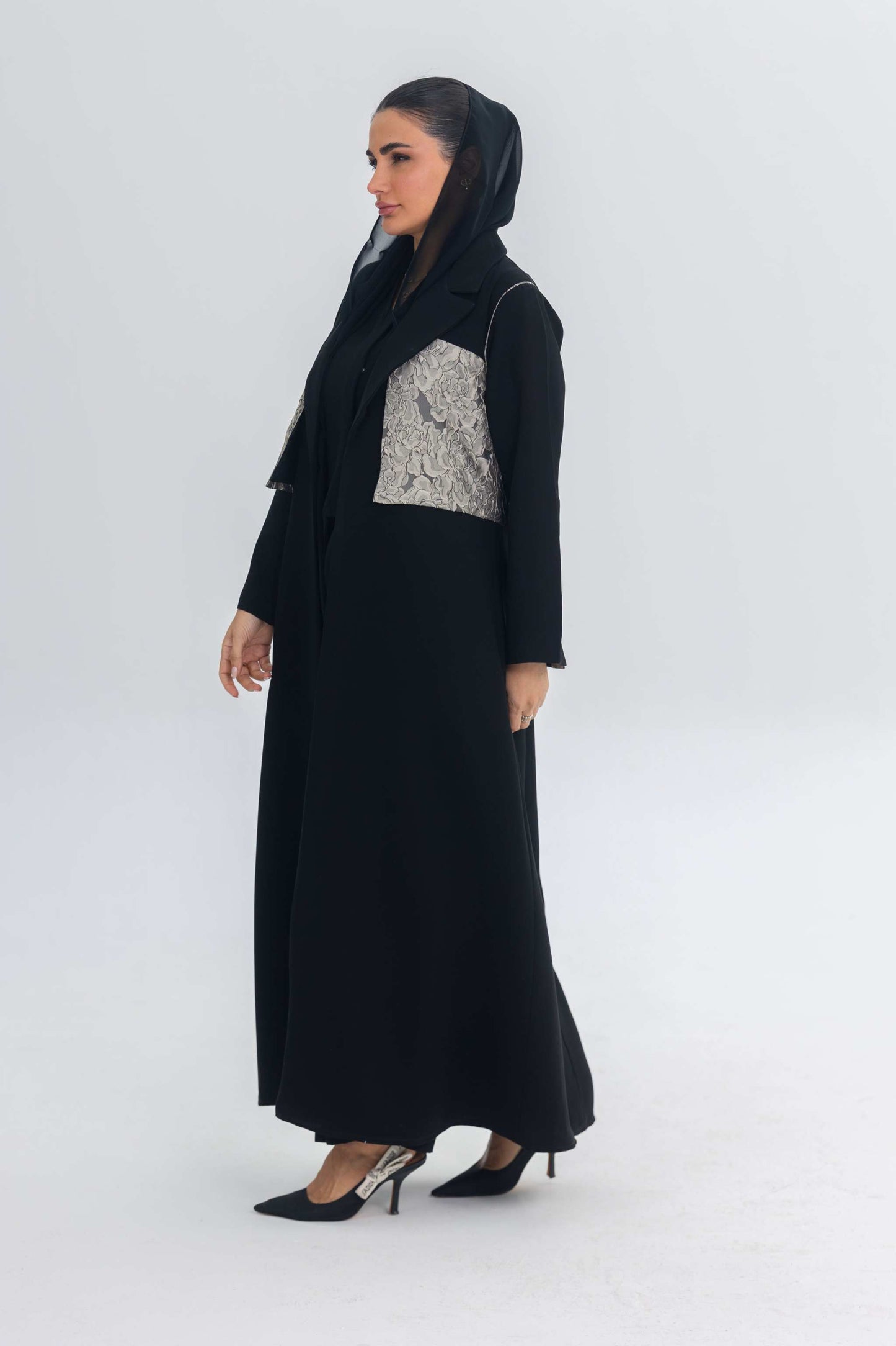 Elegant black crepe abaya with jacquard panel detail worn by woman in black heels and headscarf