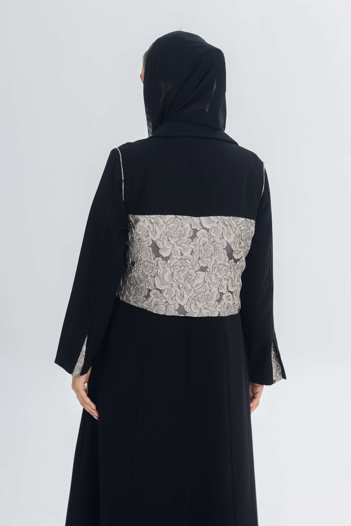 Back view of black crepe abaya featuring a textured jacquard panel and long sleeves with slit detailing.