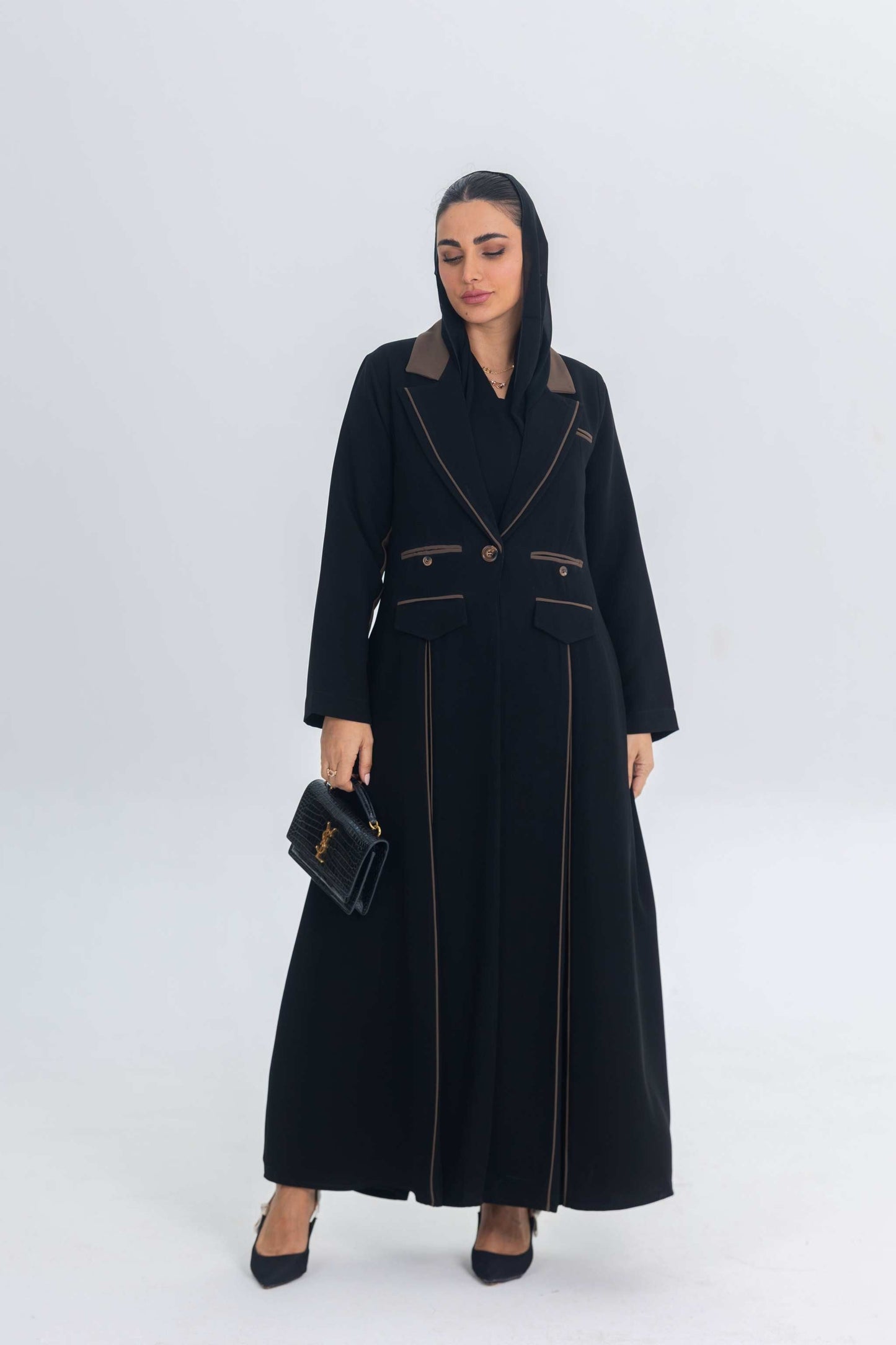 Black crepe blazer abaya with brown trim and detailing, worn with black heels and a black handbag.