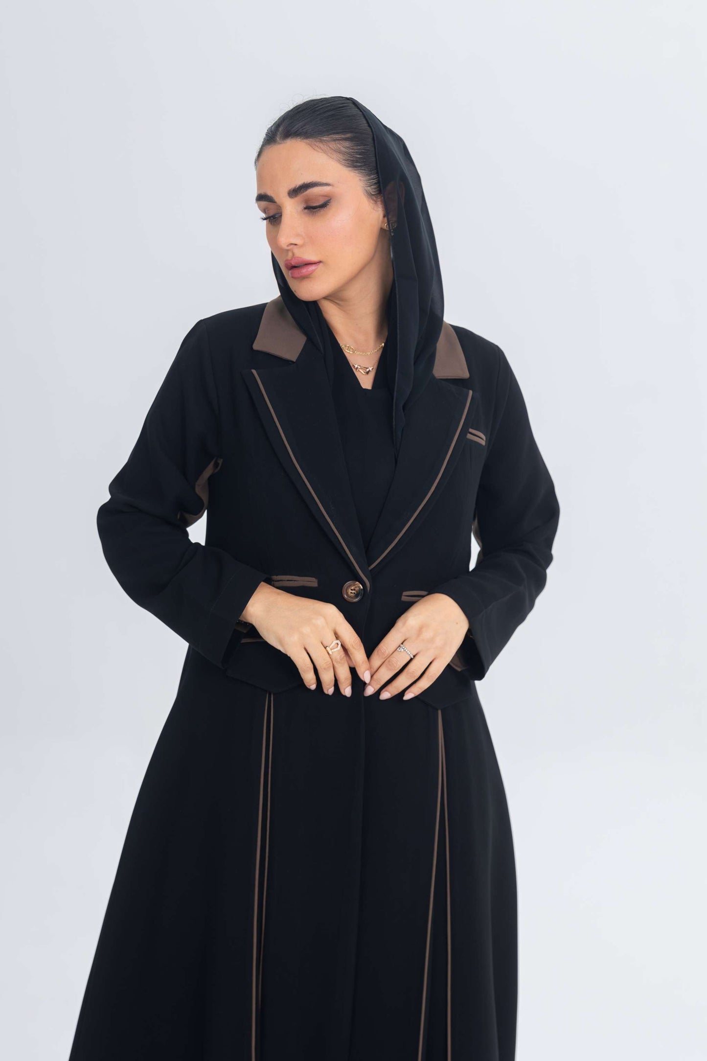 Black crepe blazer abaya with brown detailing and refined chestnut glow accents, styled on a woman with a sleek silhouette.