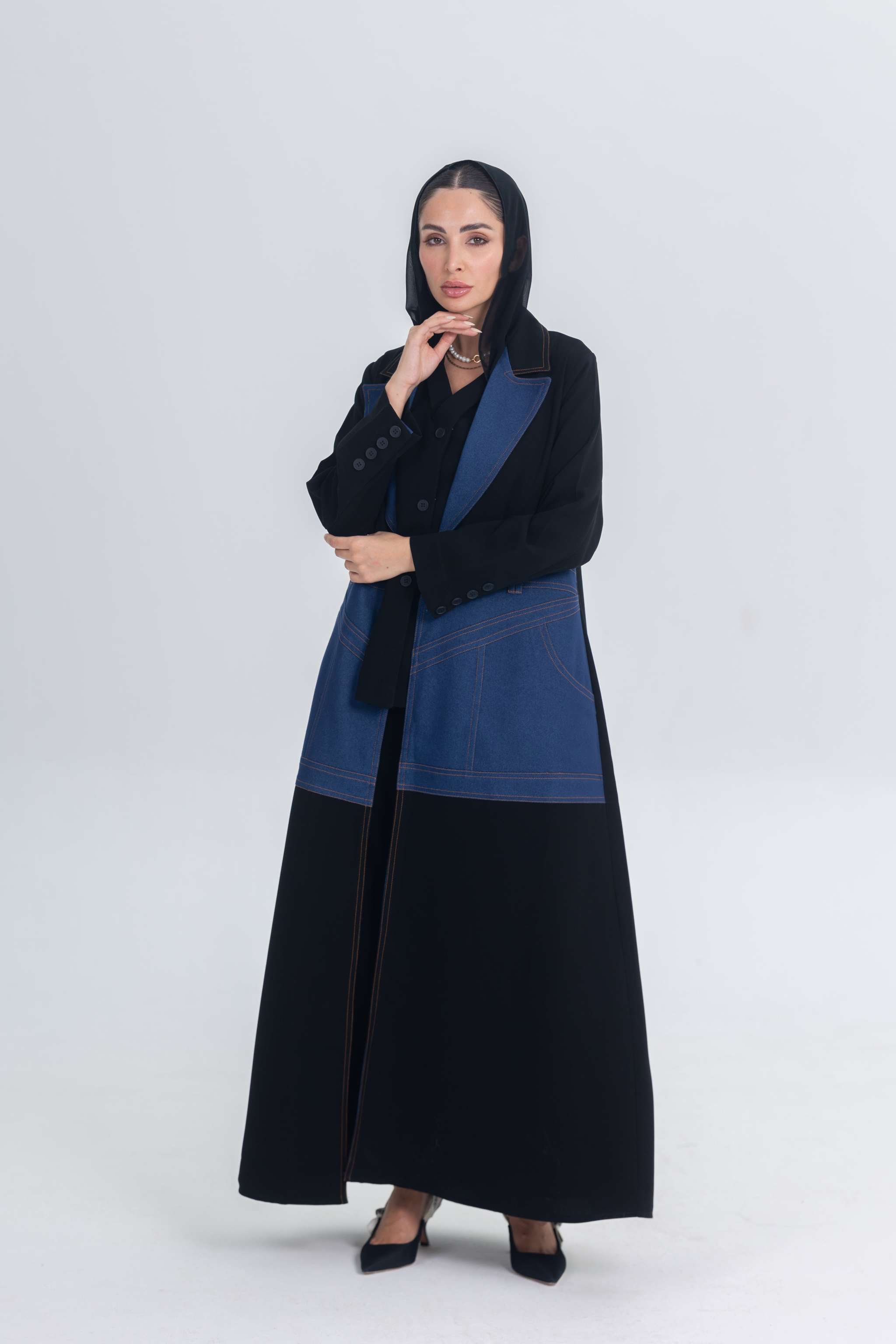 Woman wearing a black crepe abaya with denim panels, combining traditional and modern styles.