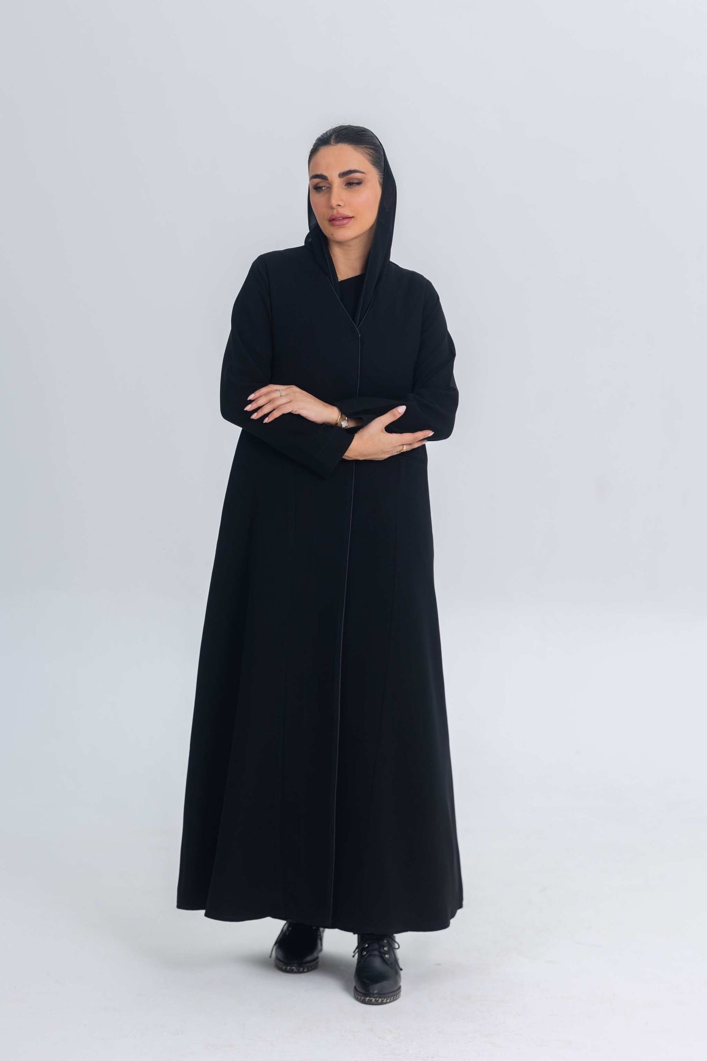 Woman wearing black crepe abaya with subtle satin details, standing against plain background