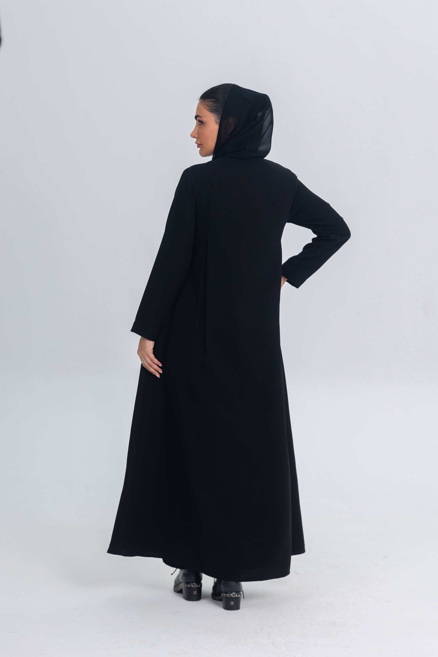 Woman wearing a black crepe abaya with subtle satin detailing, shown from the back.