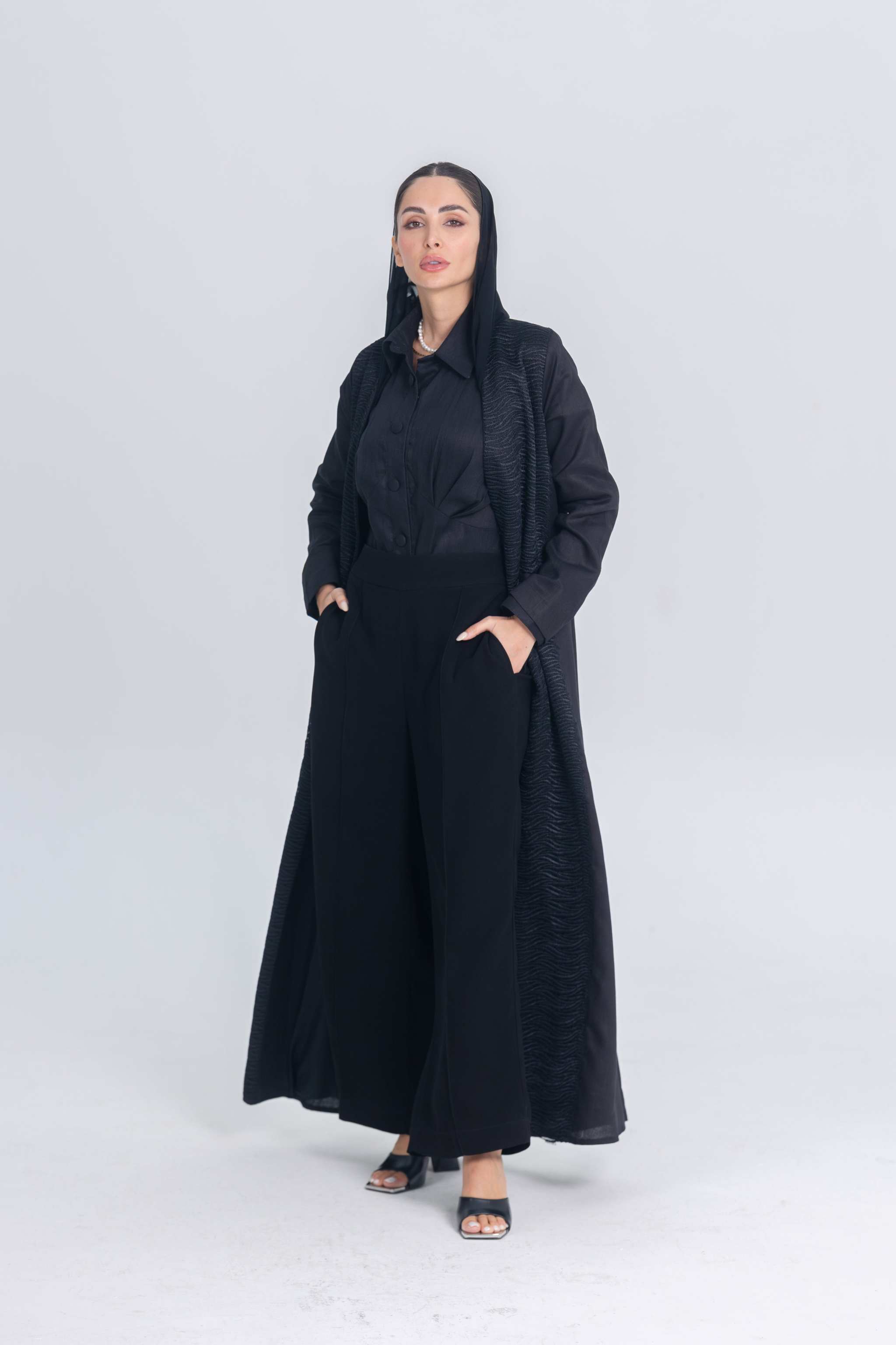 Woman wearing black linen abaya with textured fabric accents and wide-leg pants, styled for modern modest wear
