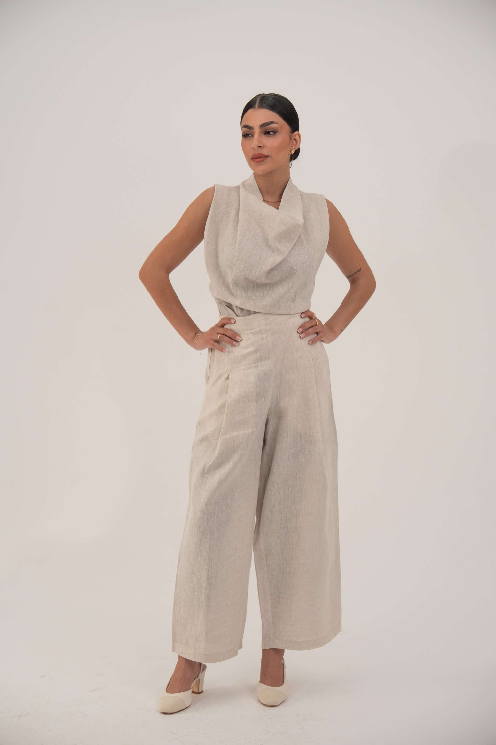 Woman wearing a sleeveless beige blouse with a draped cowl neckline and high-waisted wide-leg pants