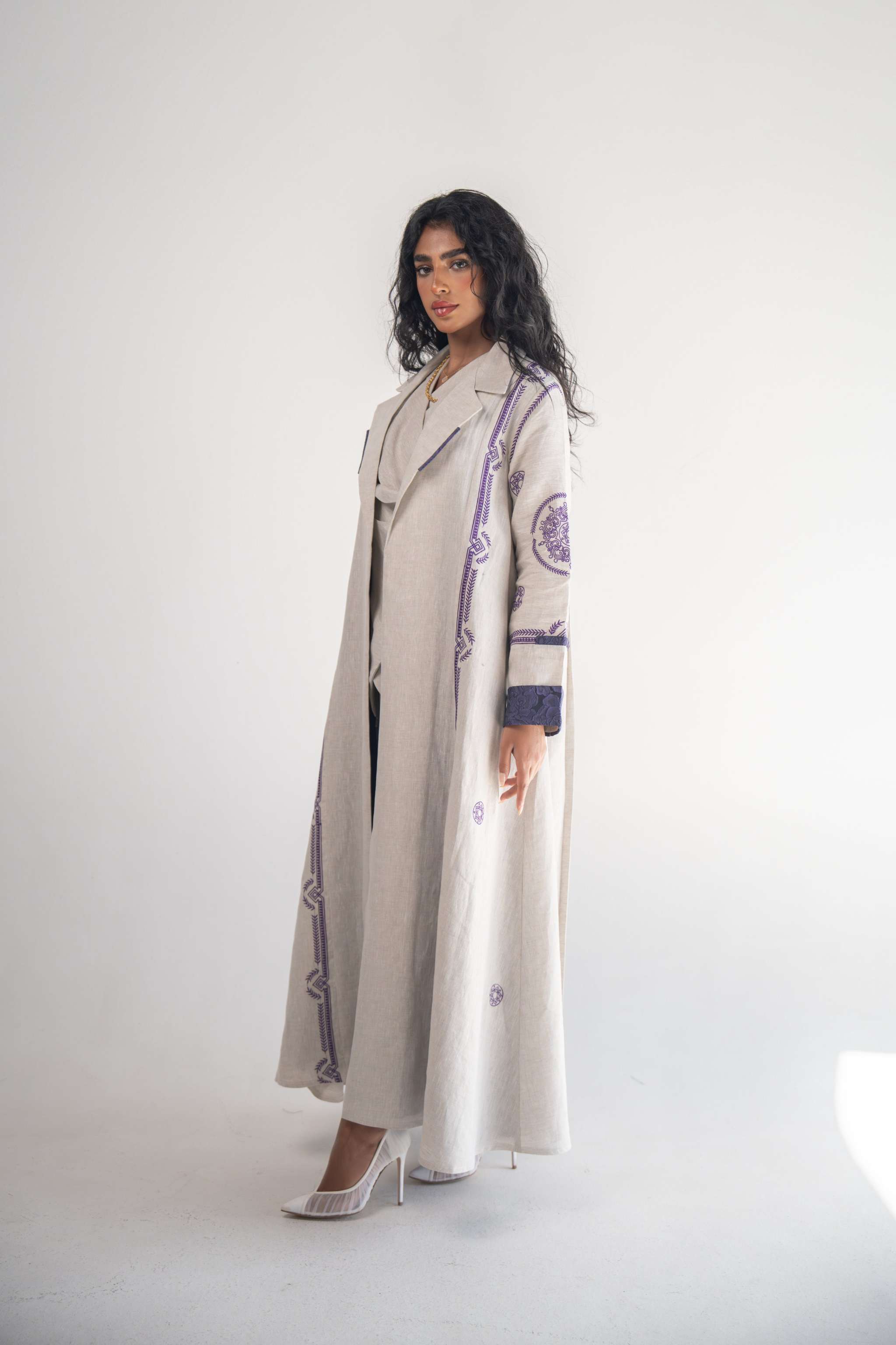 Woman wearing beige linen blazer abaya with purple geometric embroidery and chiffon inner layer
