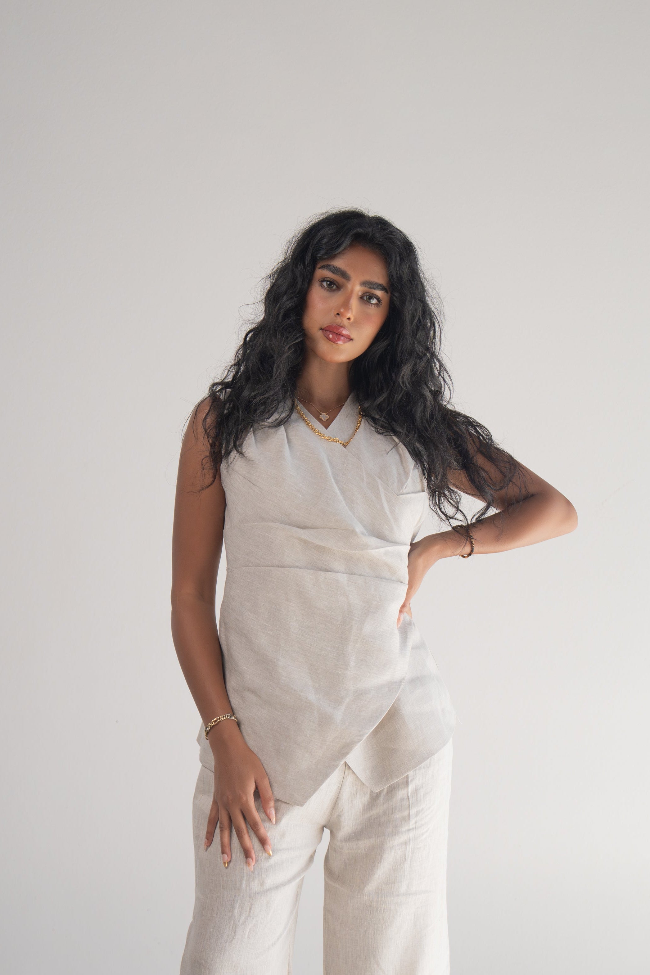 Woman wearing sleeveless almond beige blouse with wrapped front and soft pleats paired with matching wide-leg pants