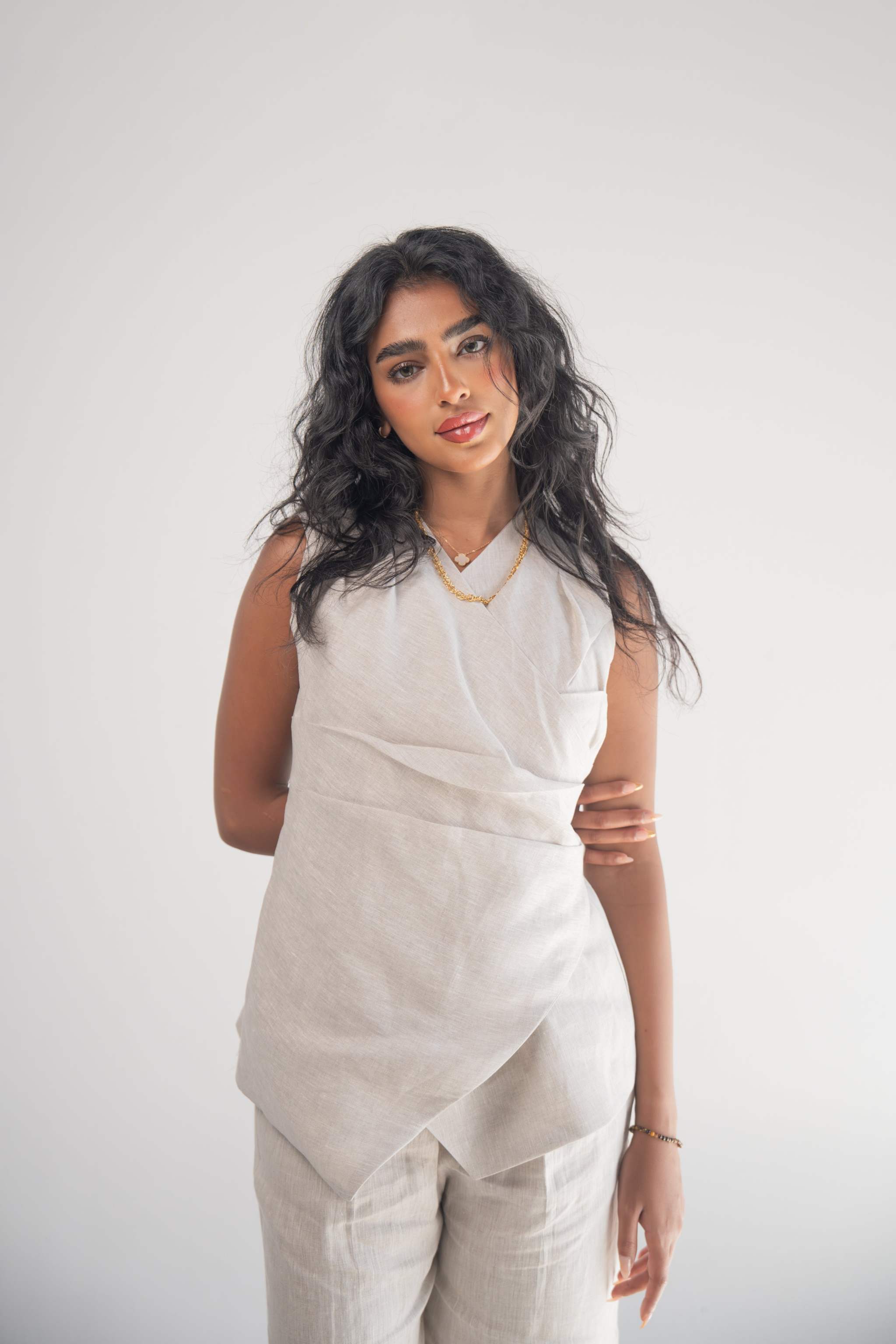 Woman wearing sleeveless Almond Beige Blouse with wrapped front and subtle pleated hem detail.