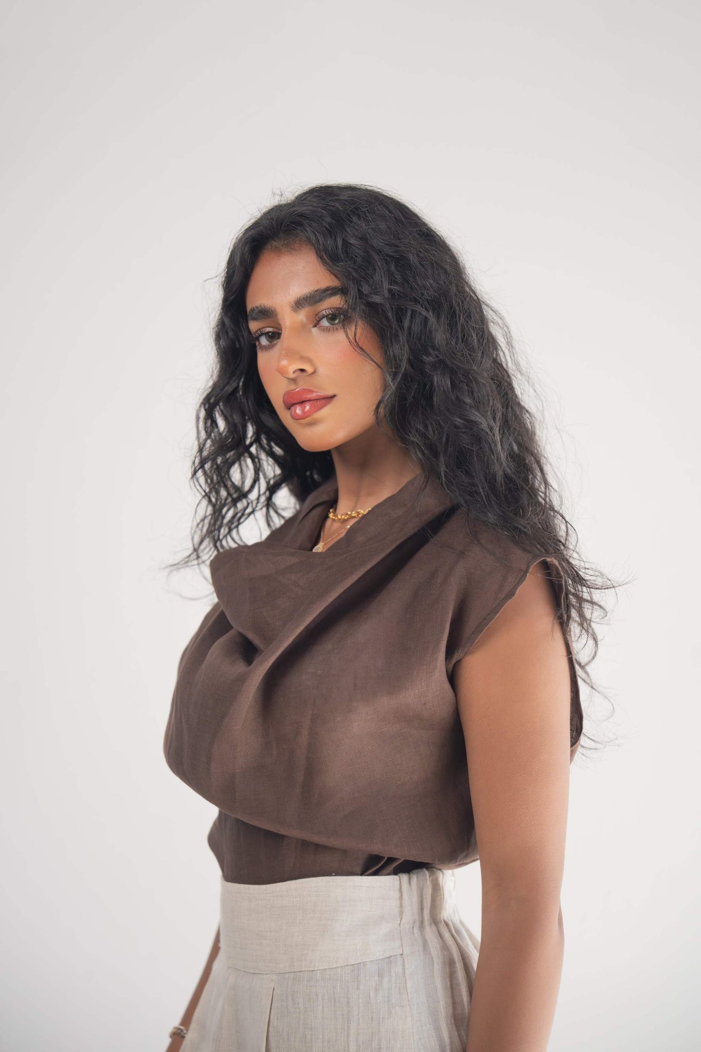 Woman wearing a sleeveless cocoa linen blouse with a draped neckline and subtle pleats