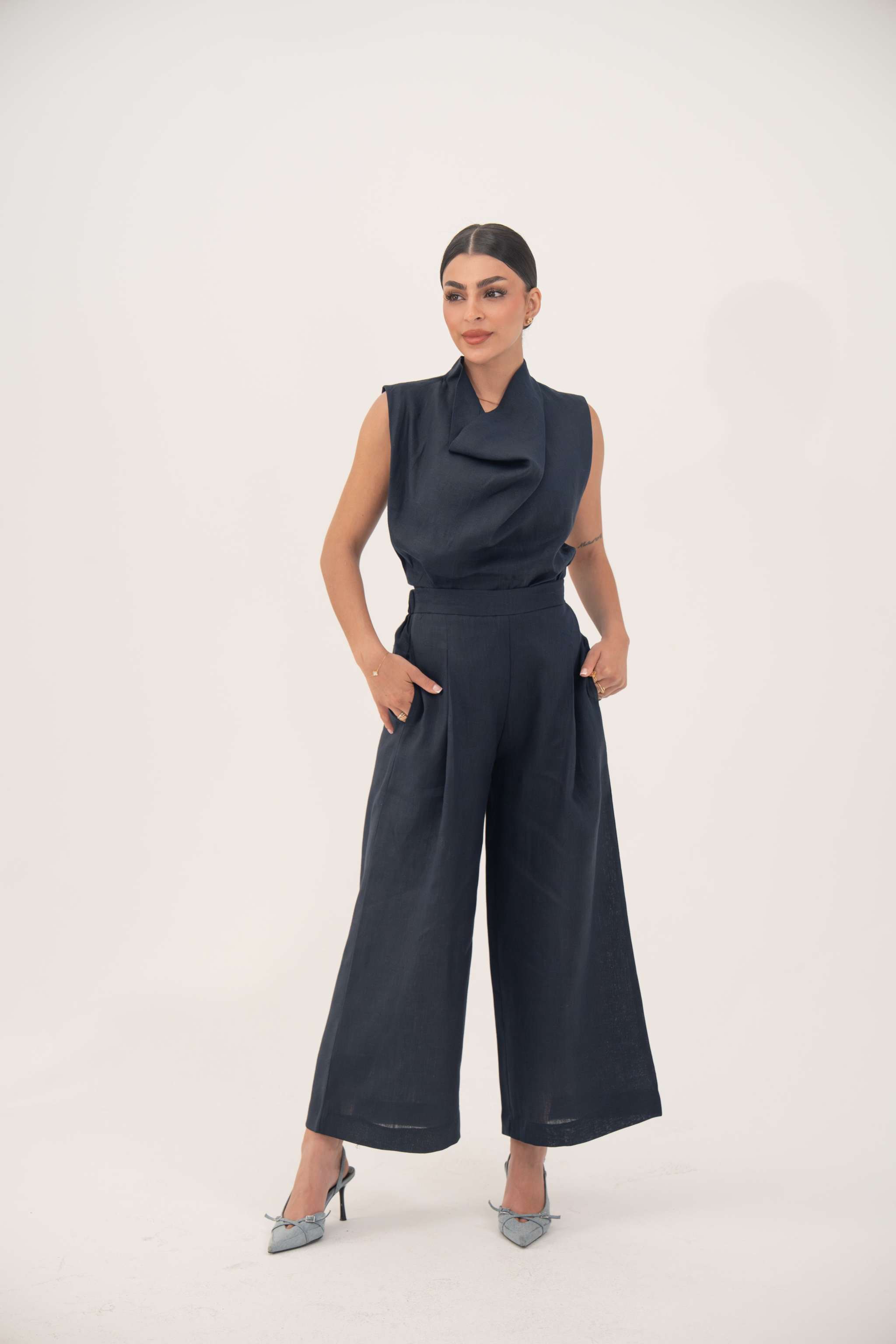 Woman wearing sleeveless navy blue linen-blend blouse with draped cowl neckline and high-waisted wide-leg pants