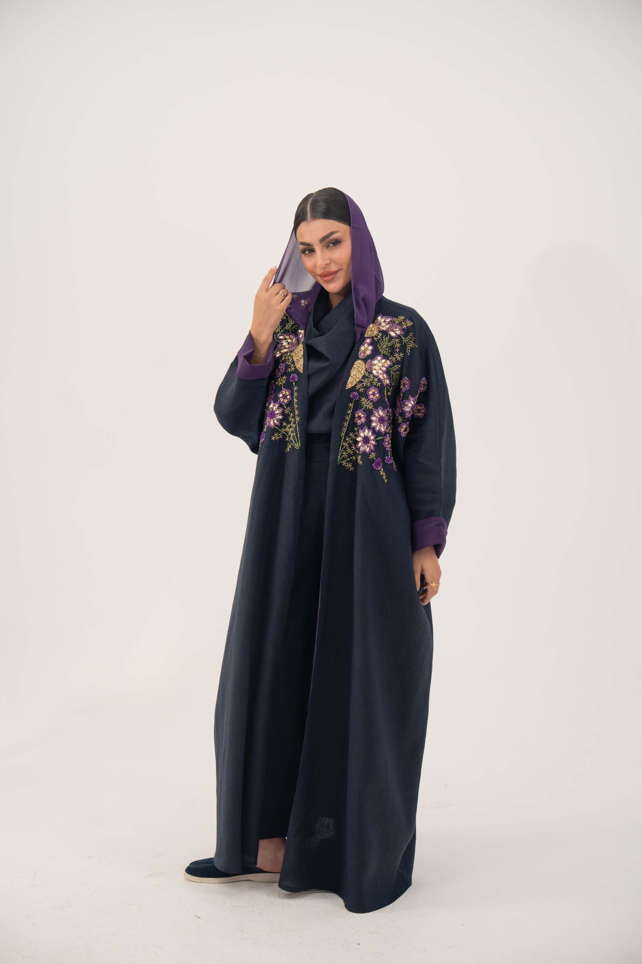 woman wearing navy blue linen-blend abaya with purple, gold, and green hand-stitched floral details and purple cuffs