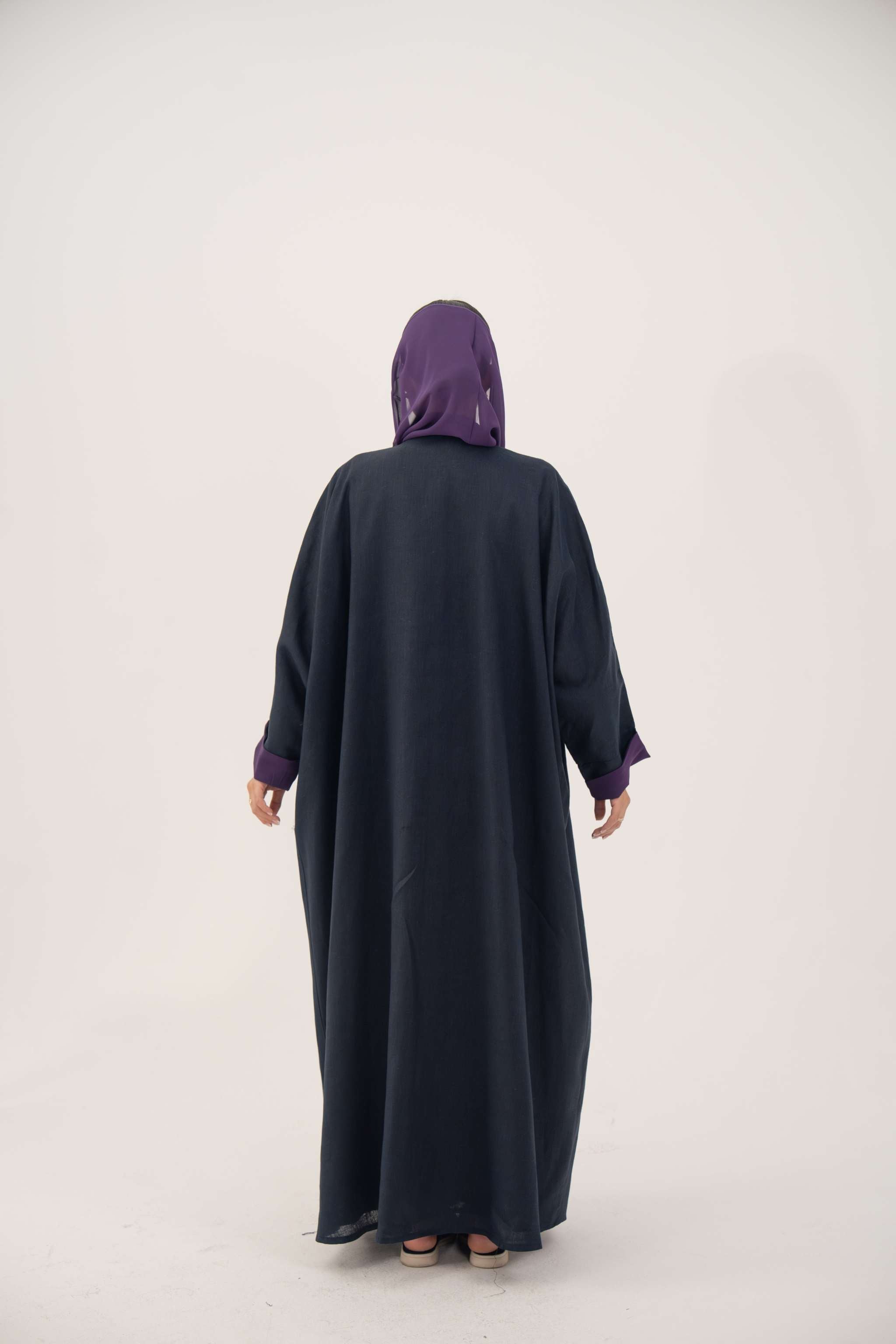 Back view of a navy blue linen-blend abaya with purple cuffs and a matching inner border, featuring a loose bisht style and lightweight lining.