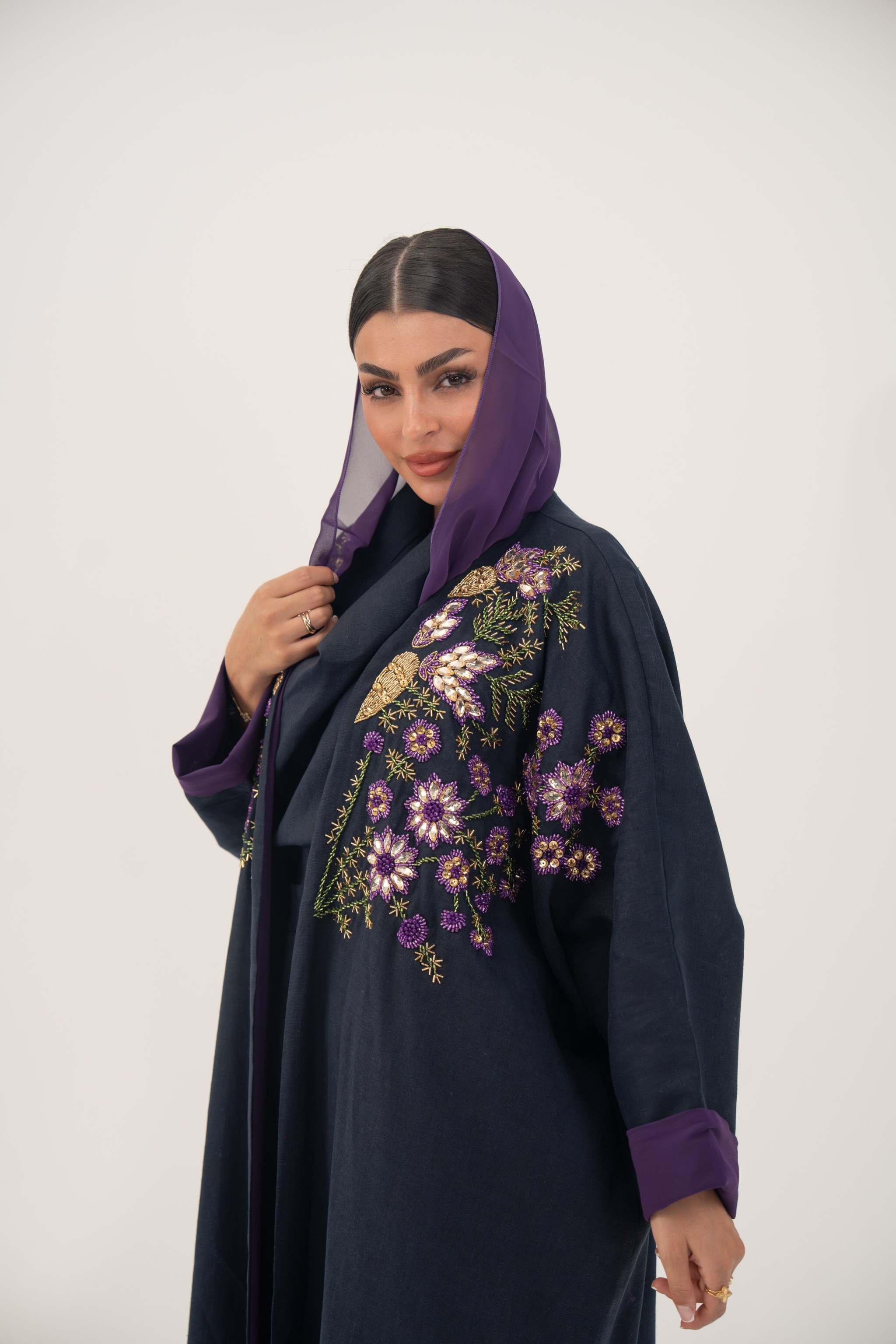 woman wearing navy blue linen-blend abaya with purple, gold, and green hand-stitched floral embroidery and purple cuffs