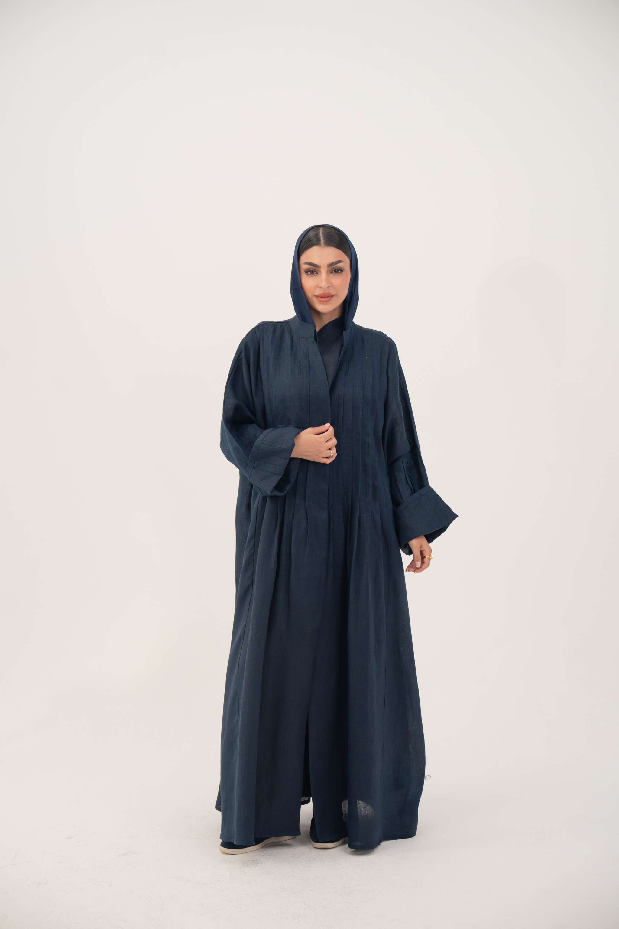 Woman wearing deep navy blue full-length open-front abaya made from lightweight linen with vertical stitched pleats and a minimalist design