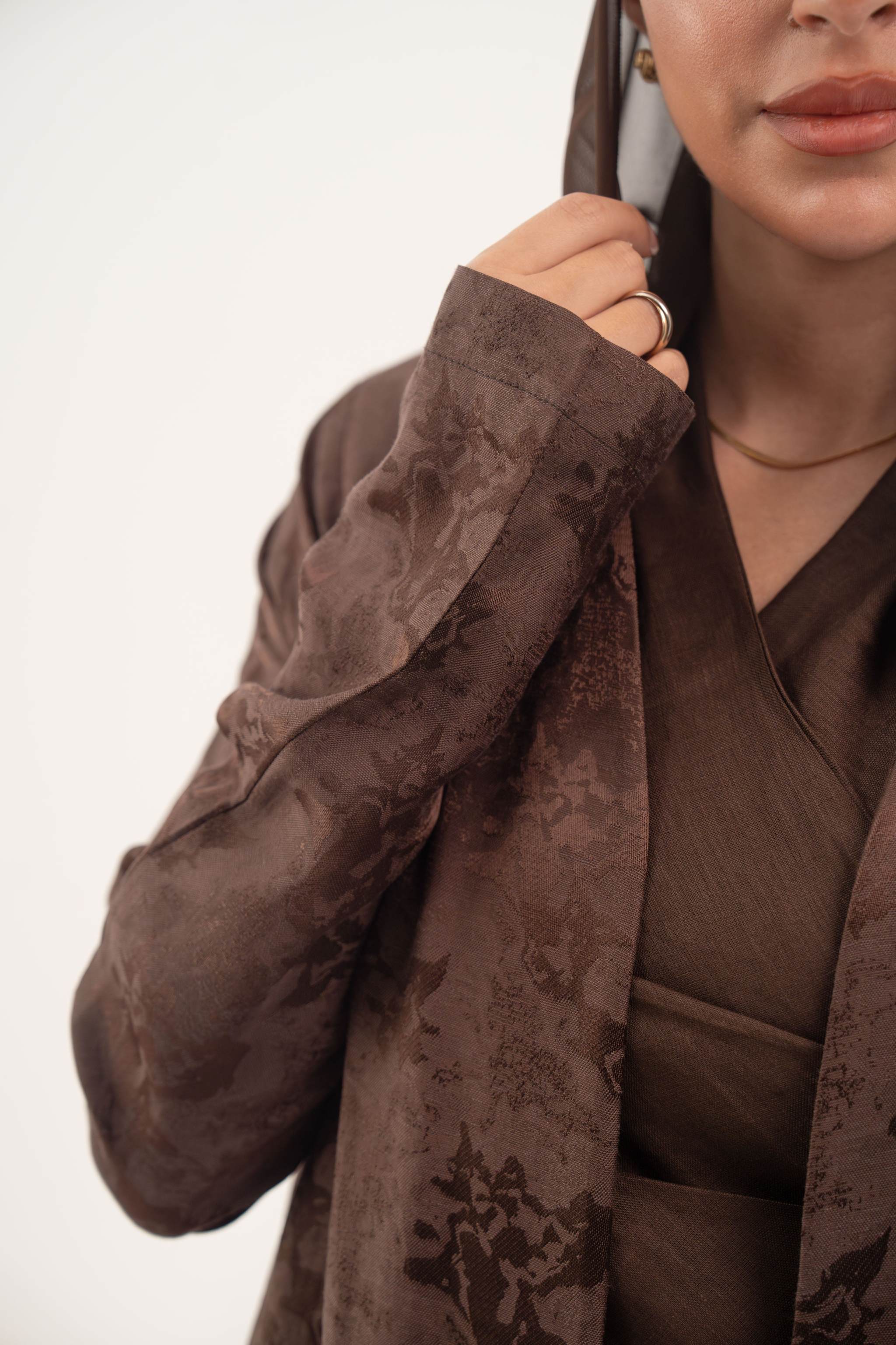 Close-up of a warm cocoa brown jacquard silk abaya with subtle woven floral pattern and long sleeves.