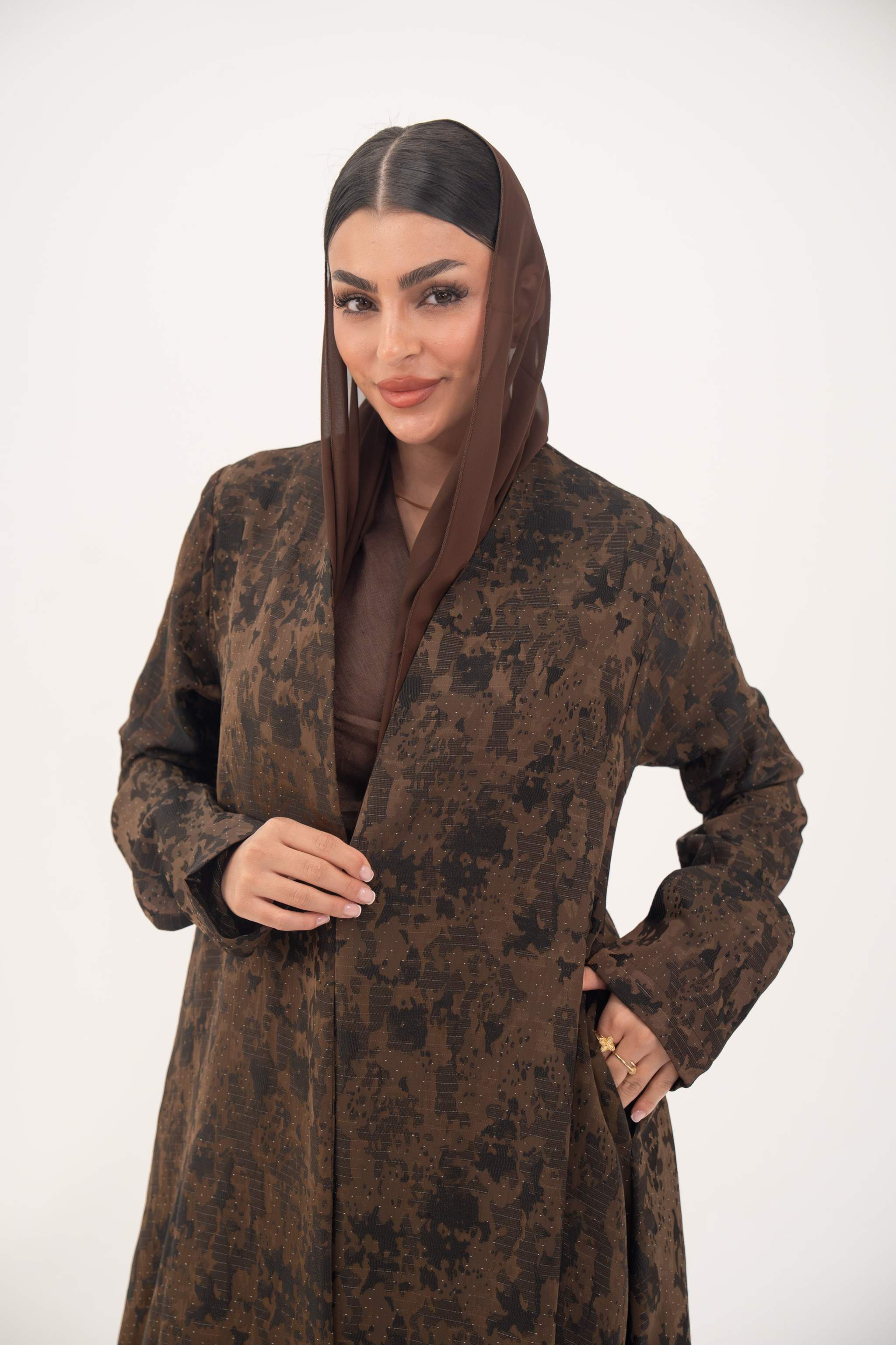 Woman wearing a lightweight espresso brown jacquard silk abaya with subtle tonal pattern, open front, side pockets, and full-length sleeves.